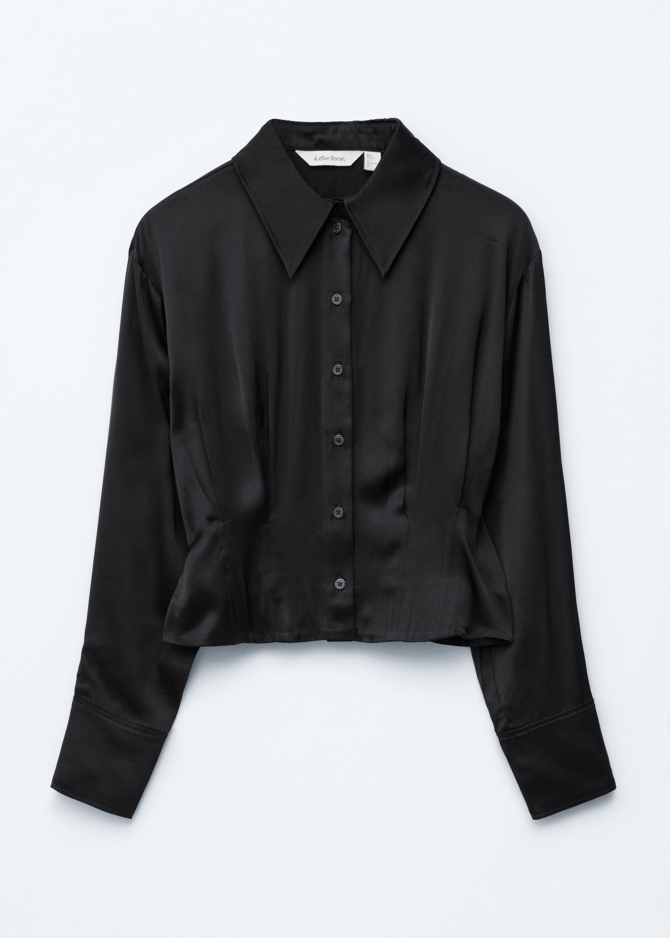 View larger image: A front-facing black satin shirt is displaying a pointed collar, a full button-front closure, and long sleeves ending in wide cuffs. The shirt is featuring darting at the waist, creating a cinched fit, and is cut to a cropped length.