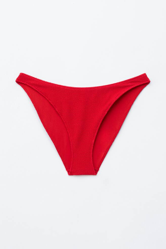 Rode bikini-slips met een lage taille tonen hun vooraanzicht. Ze zijn voorzien van een gestructureerde jacquardstof op het hoofdgedeelte, met gladde stof die de beenopeningen en gebogen taille omlijnt. - 1