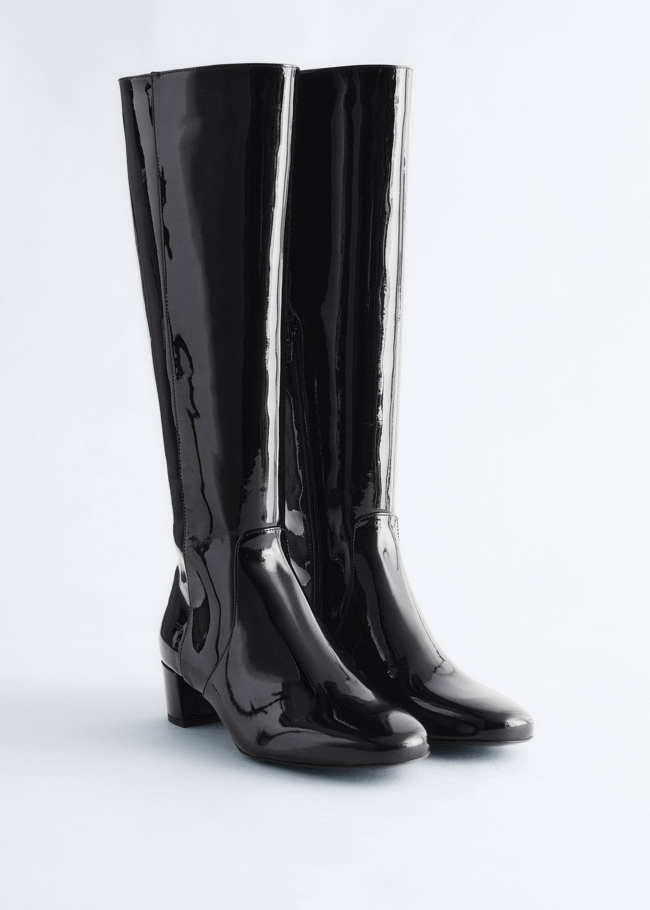 Agrandir l'image: Deux bottes noires brillantes à hauteur de genou sont debout, avec des tiges ajustées, des bouts en amande et des talons blocs. Des fermetures éclair latérales sont visibles sur les côtés intérieurs.
