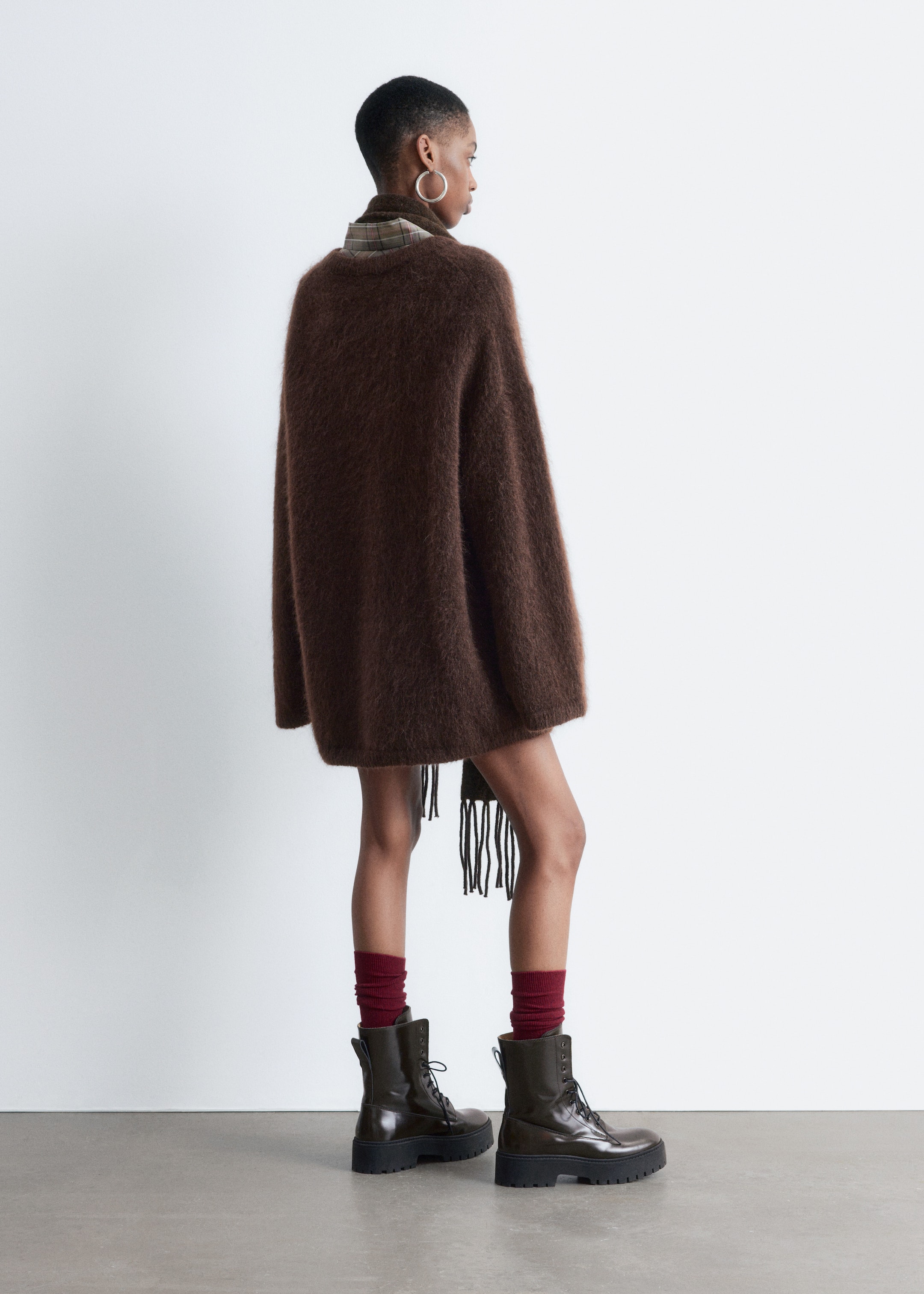 View larger image: A brown, fuzzy, oversized sweater is being presented from its back right side. It is featuring a loose, tunic-length fit with wide sleeves. A plaid collar is visible at the neckline, and a dark fringed detail is hanging from its lower left side.