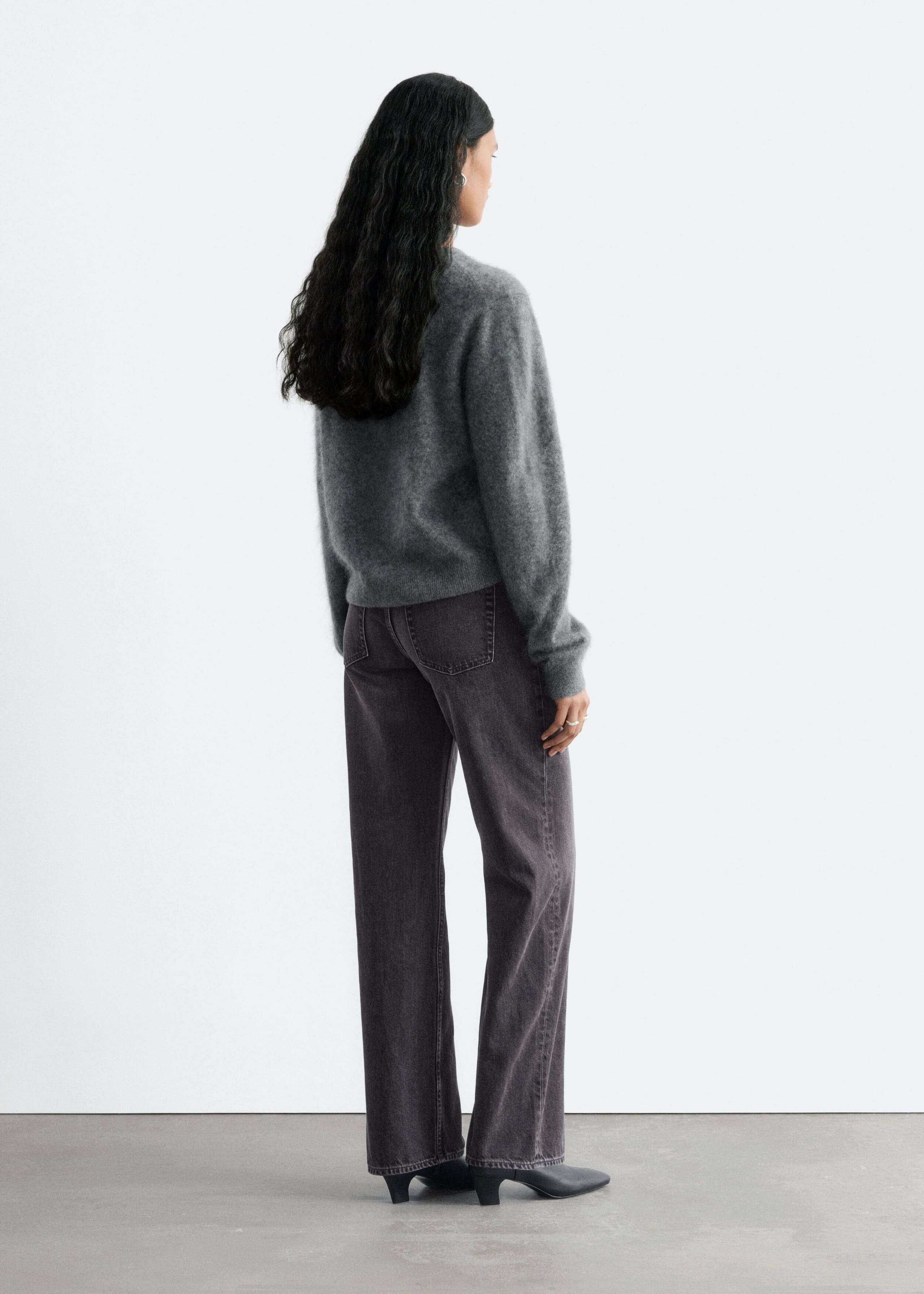 The model is wearing faded dark gray straight-leg jeans and is standing with their back to the camera. The jeans feature a regular fit with classic back patch pockets and are styled with a fuzzy gray sweater and black heeled boots.
