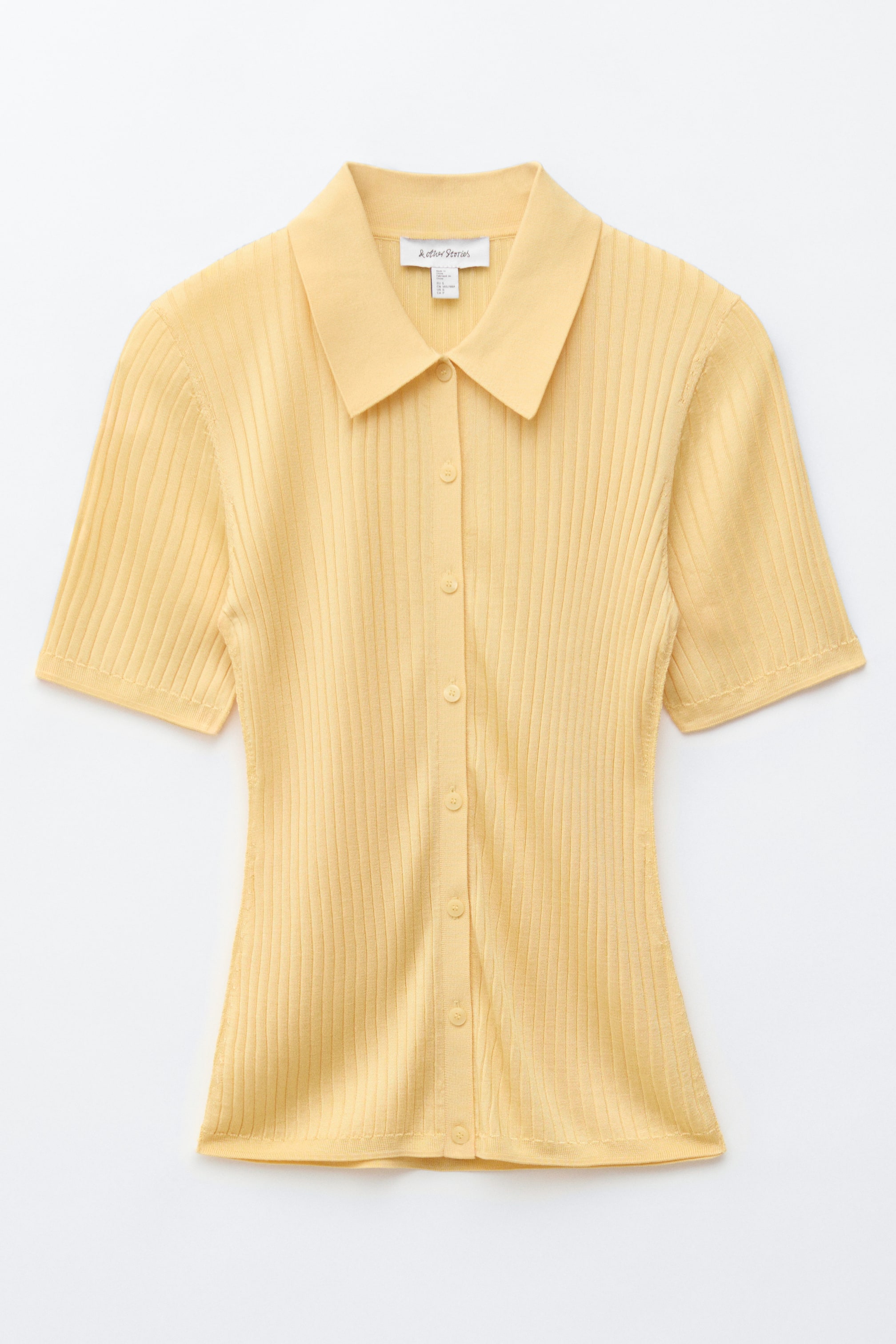 הצגת תמונה גדולה יותר: חולצת ריב-סרג. חולצת ריב-סרג בצבע צהוב בהיר מציגה צווארון מחודד ושרוולים קצרים מקדימה. פתח כפתורים מלא עם כפתורים תואמים בצבע צהוב בהיר עובר לאורך המרכז, ומדגיש את המרקם האנכי של הבגד.