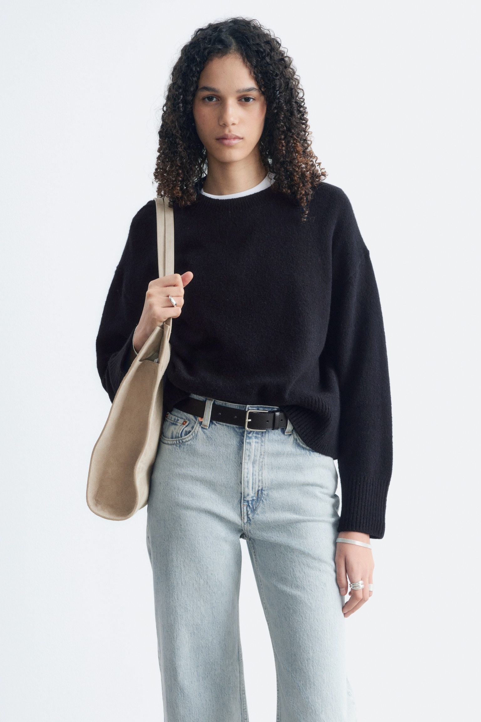 Un pull en maille noir à manches longues est présenté de face, mettant en valeur une silhouette décontractée. Il est conçu avec un col rond côtelé, des poignets côtelés et un ourlet côtelé. - 1