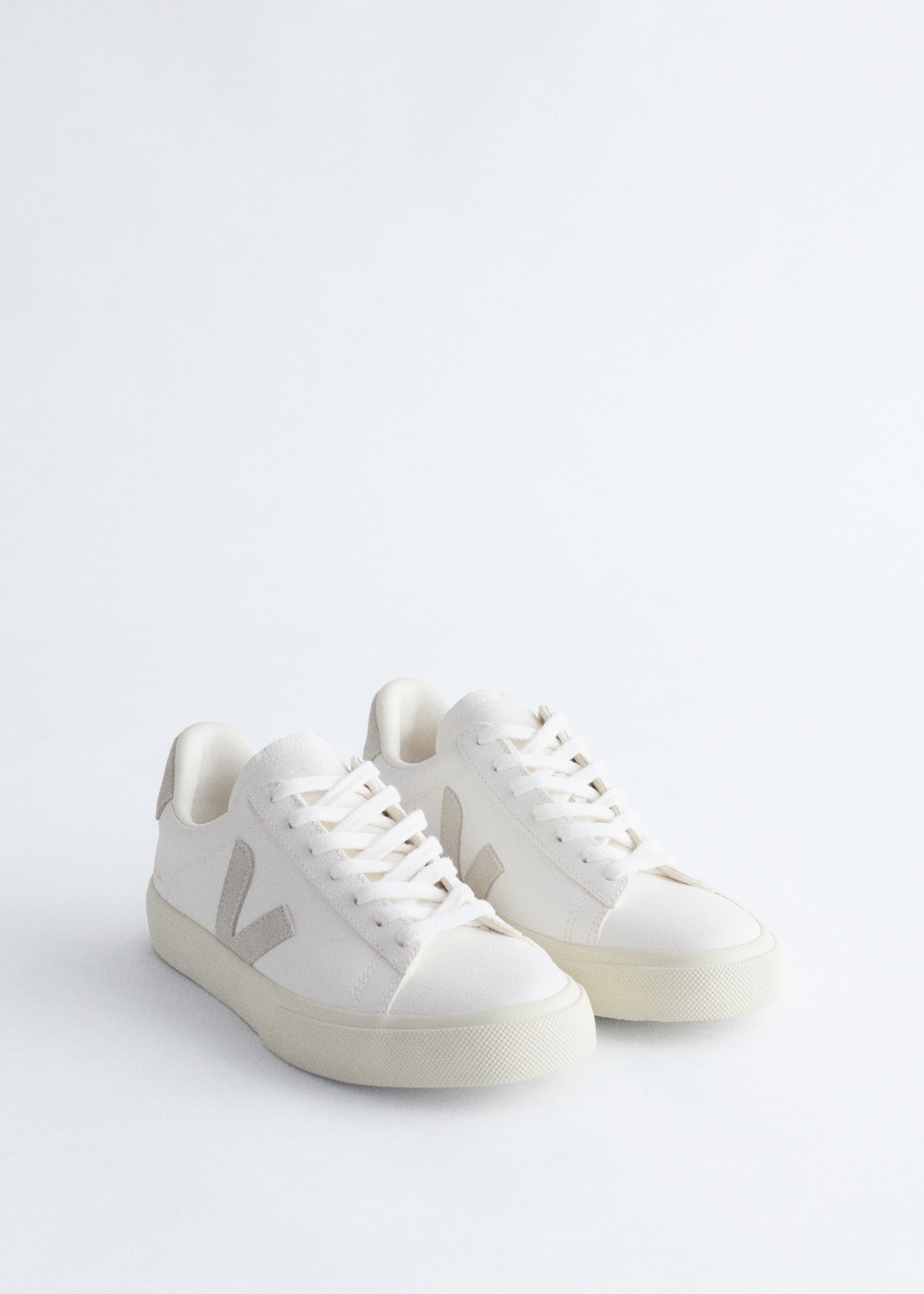 Ver imagen más grande: Un par de zapatillas de color blanco roto se están presentando, con cordones blancos, un logo 'V' en contraste de color gris claro en el lateral y pestañas en el talón a juego en gris claro. Están descansando sobre sus suelas de goma blanco roto, inclinadas ligeramente hacia adelante para revelar sus secciones frontales.