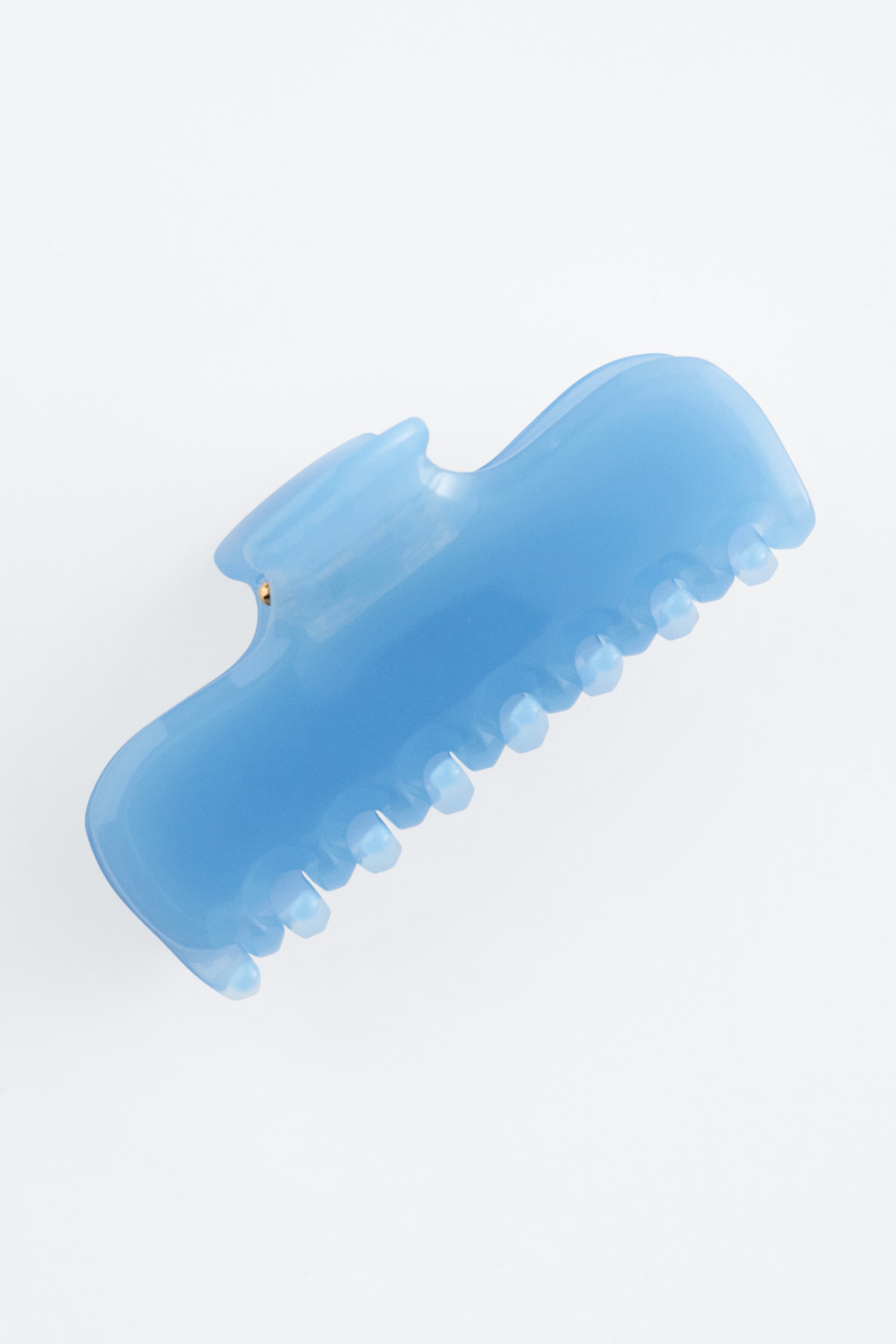 Grotere afbeelding bekijken: Een lichtblauwe doorschijnende haarclip wordt gepresenteerd, met een gebogen bovenkant en in elkaar grijpende tanden langs de onderste randen. Aan één kant is een kleine gouden scharnierpen zichtbaar.