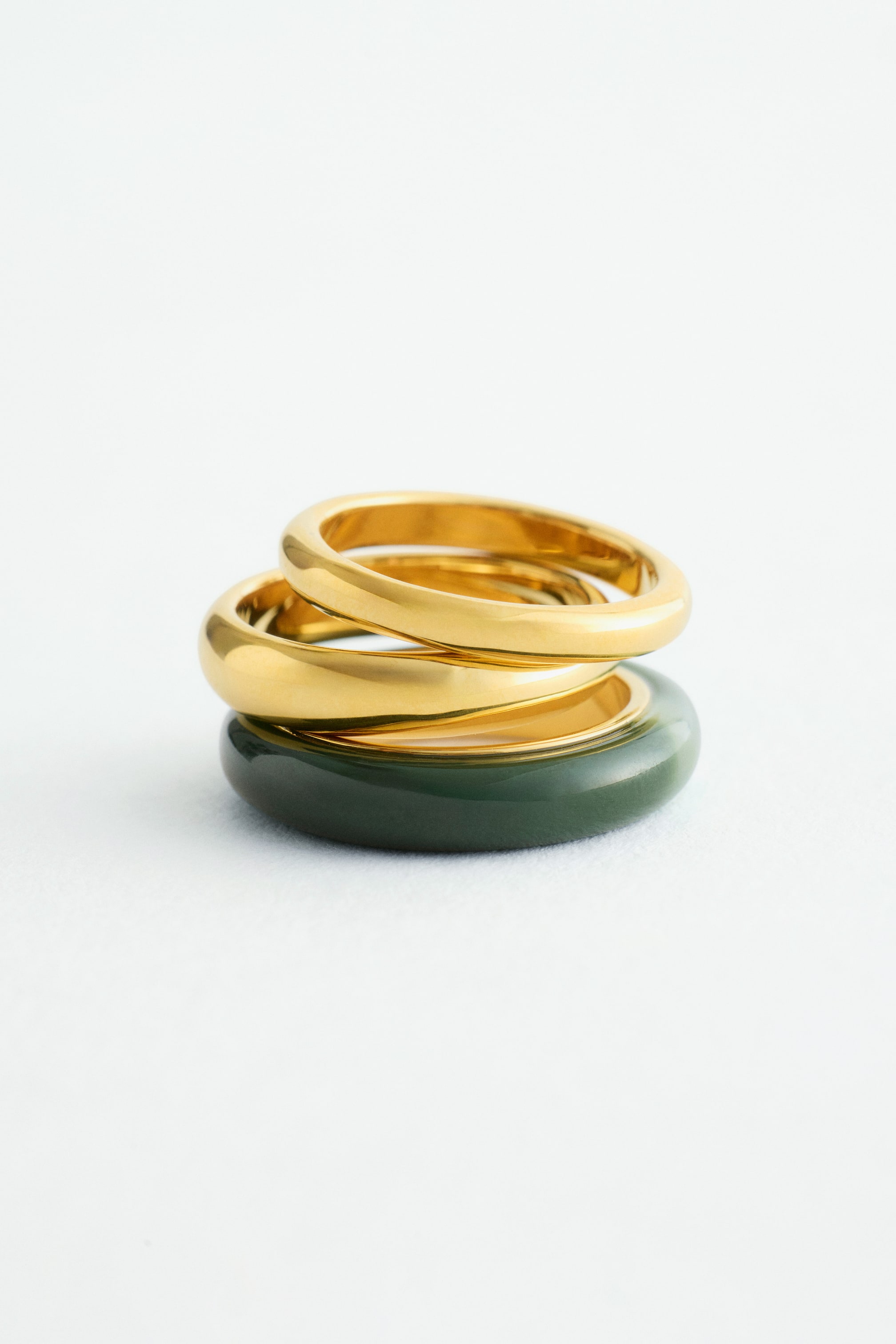 Größeres Bild anzeigen: Ein Set aus drei Ringen wird in der Vorderansicht präsentiert, wobei zwei goldene Messingringe mit hochglänzendem Finish auf einem kontrastierenden dunkelgrünen Band gestapelt sind.