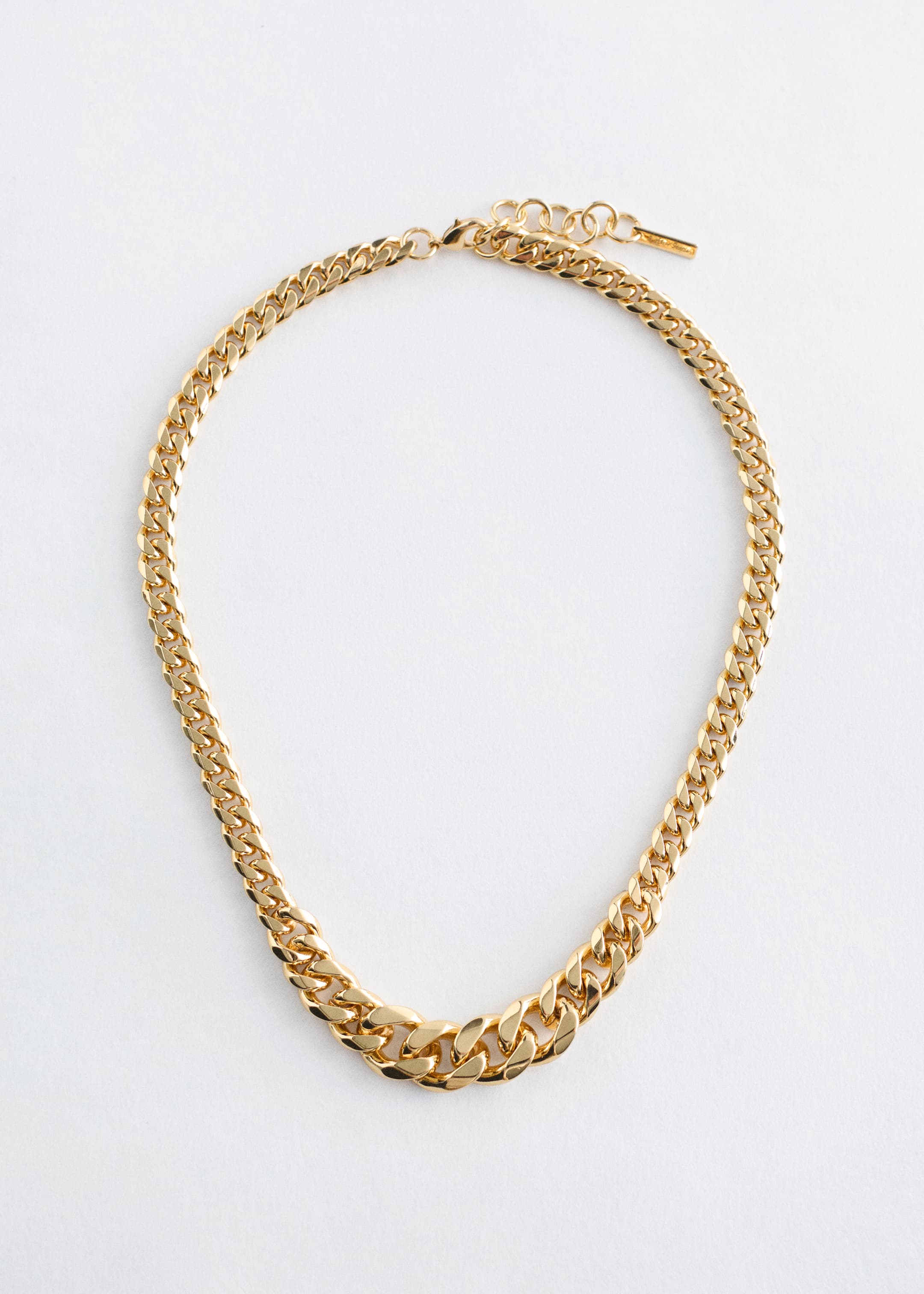 Ingrandisci l'immagine: Una collana corta in ottone lucido presenta un design simmetrico con maglie a catena che diventano progressivamente più spesse verso il centro. È caratterizzata da una lunghezza regolabile e una chiusura a moschettone.
