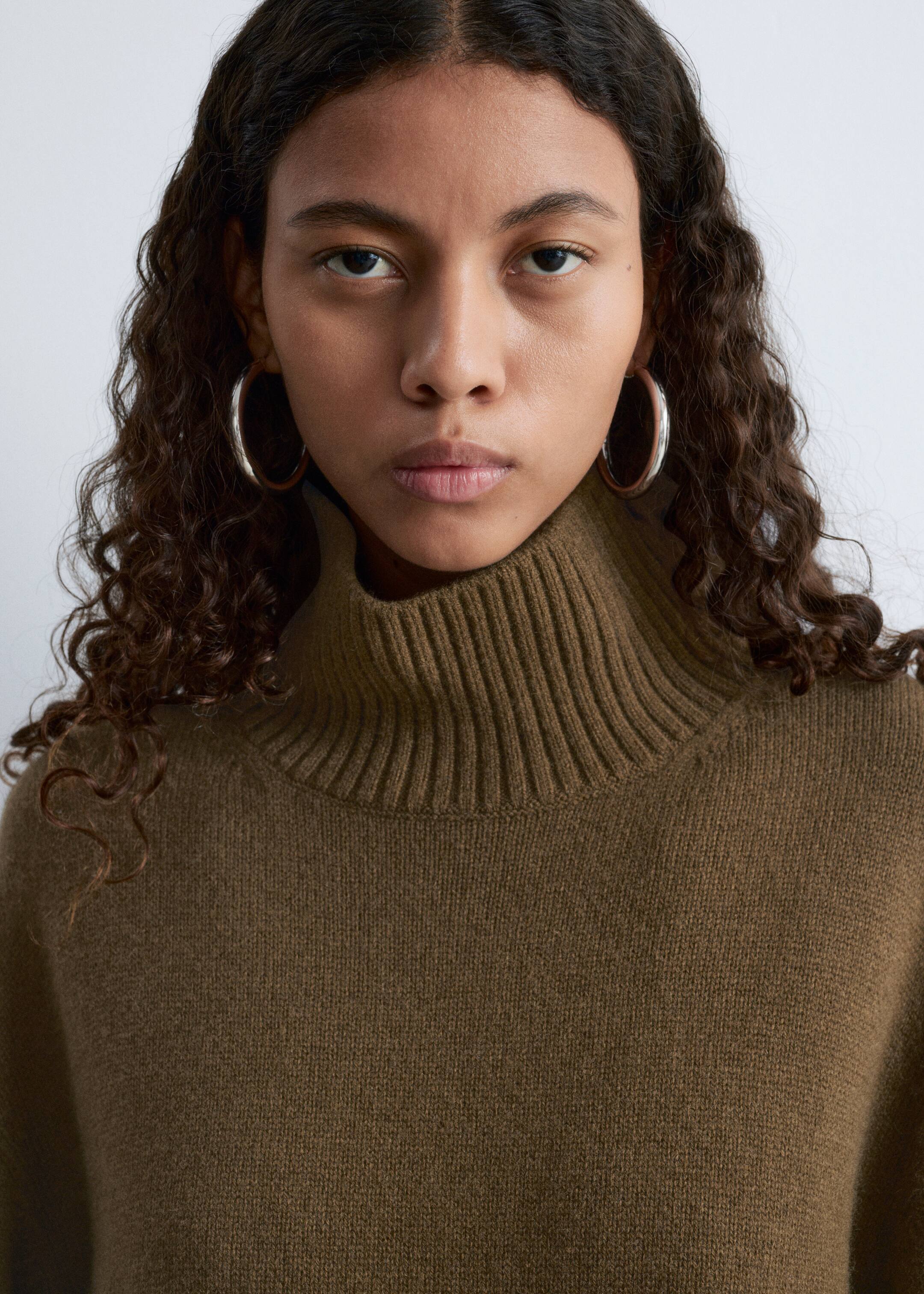 Agrandir l'image: Un pull à col roulé brun olive est porté, avec un col haut côtelé et une texture lisse en maille fine.
