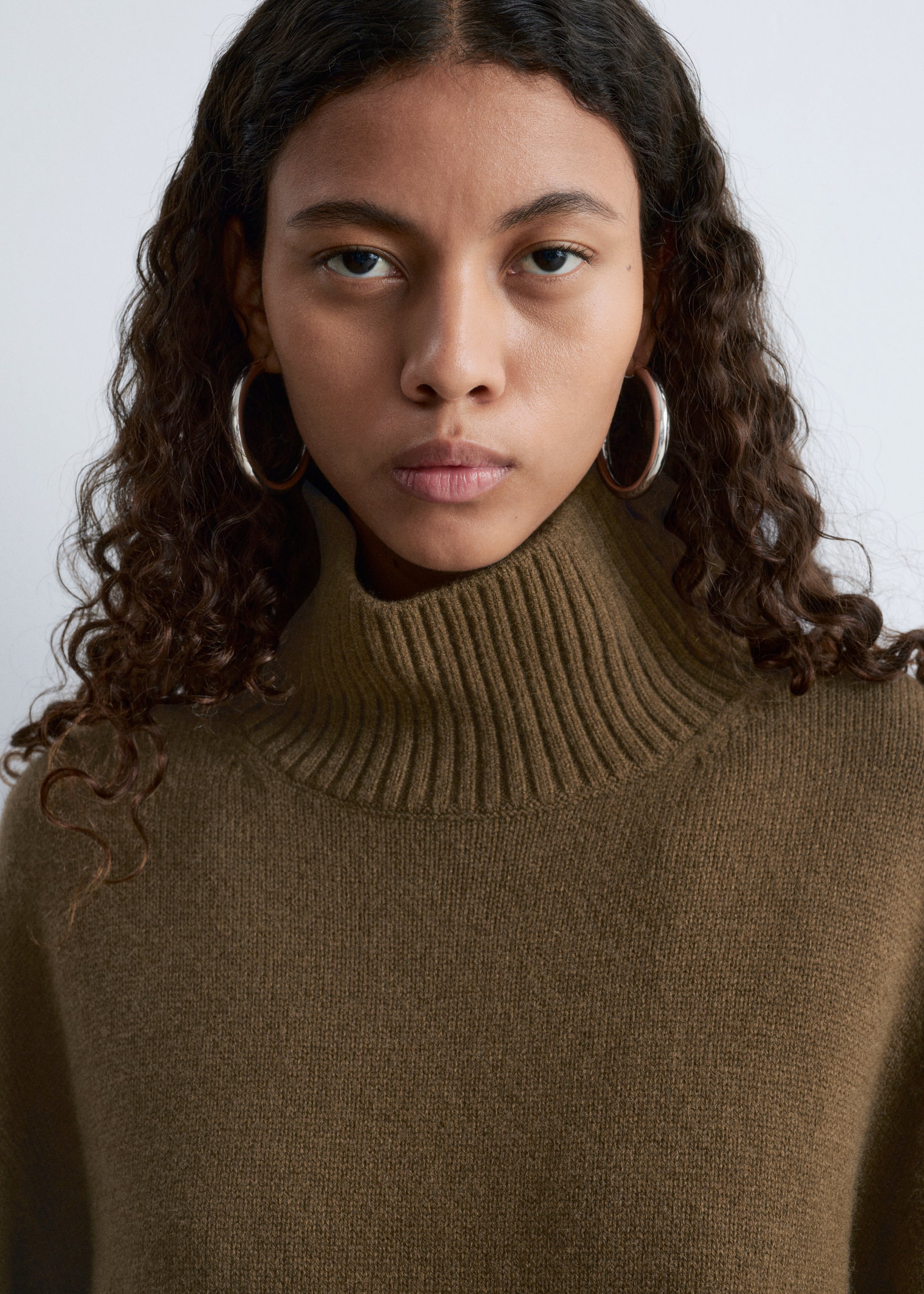 Größeres Bild ansehen: Ein olivbrauner Rollkragenpullover wird getragen, der sich durch einen hohen, gerippten Kragen und eine glatte, feinstrickige Textur auszeichnet.