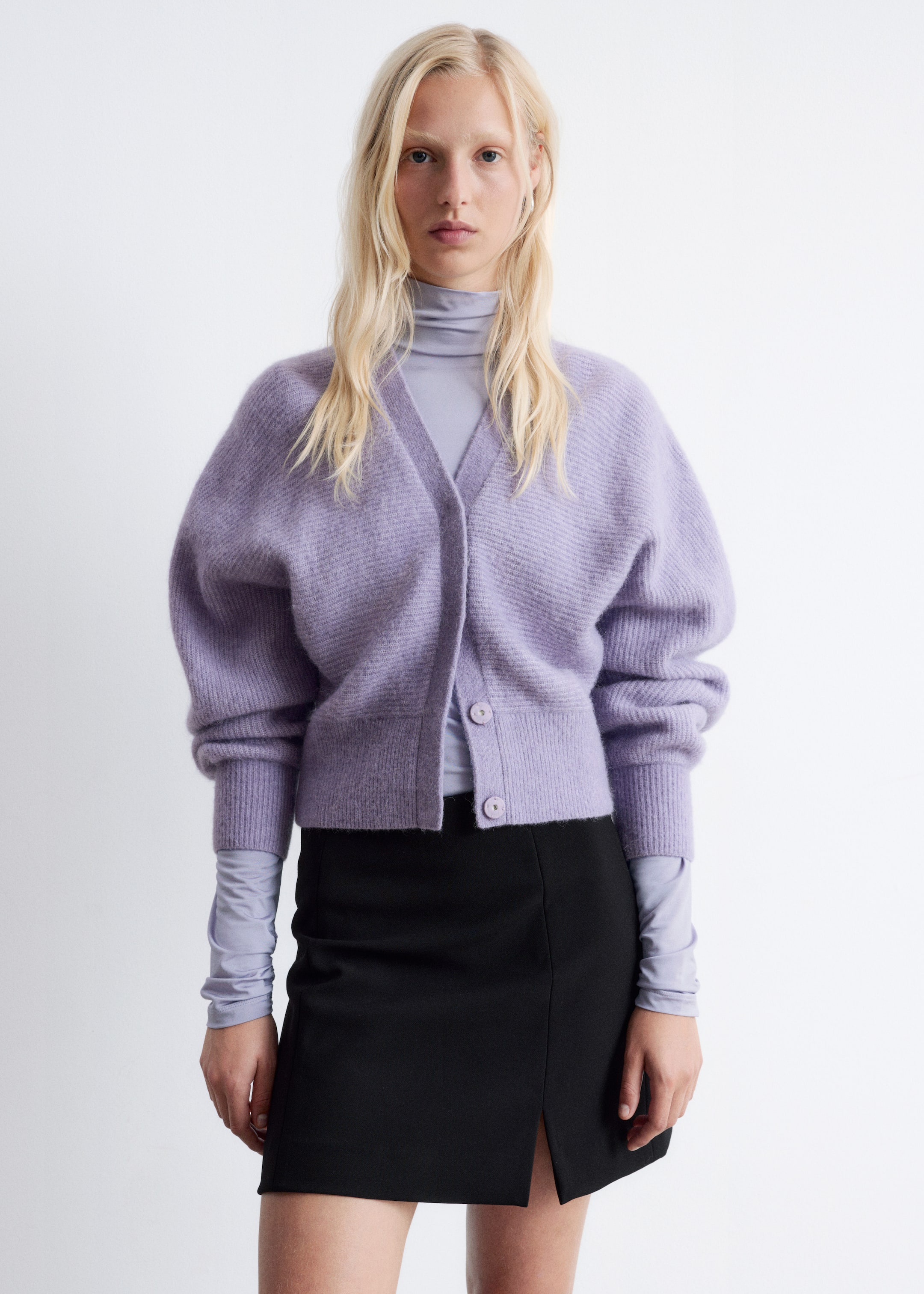 Agrandir l'image: Un cardigan court en mélange d'alpaga lavande est porté par le mannequin, superposé à un haut à col roulé violet clair. Le cardigan se distingue par un col en V, trois boutons ronds fermés, et des poignets et un ourlet côtelés avec des manches complètes.