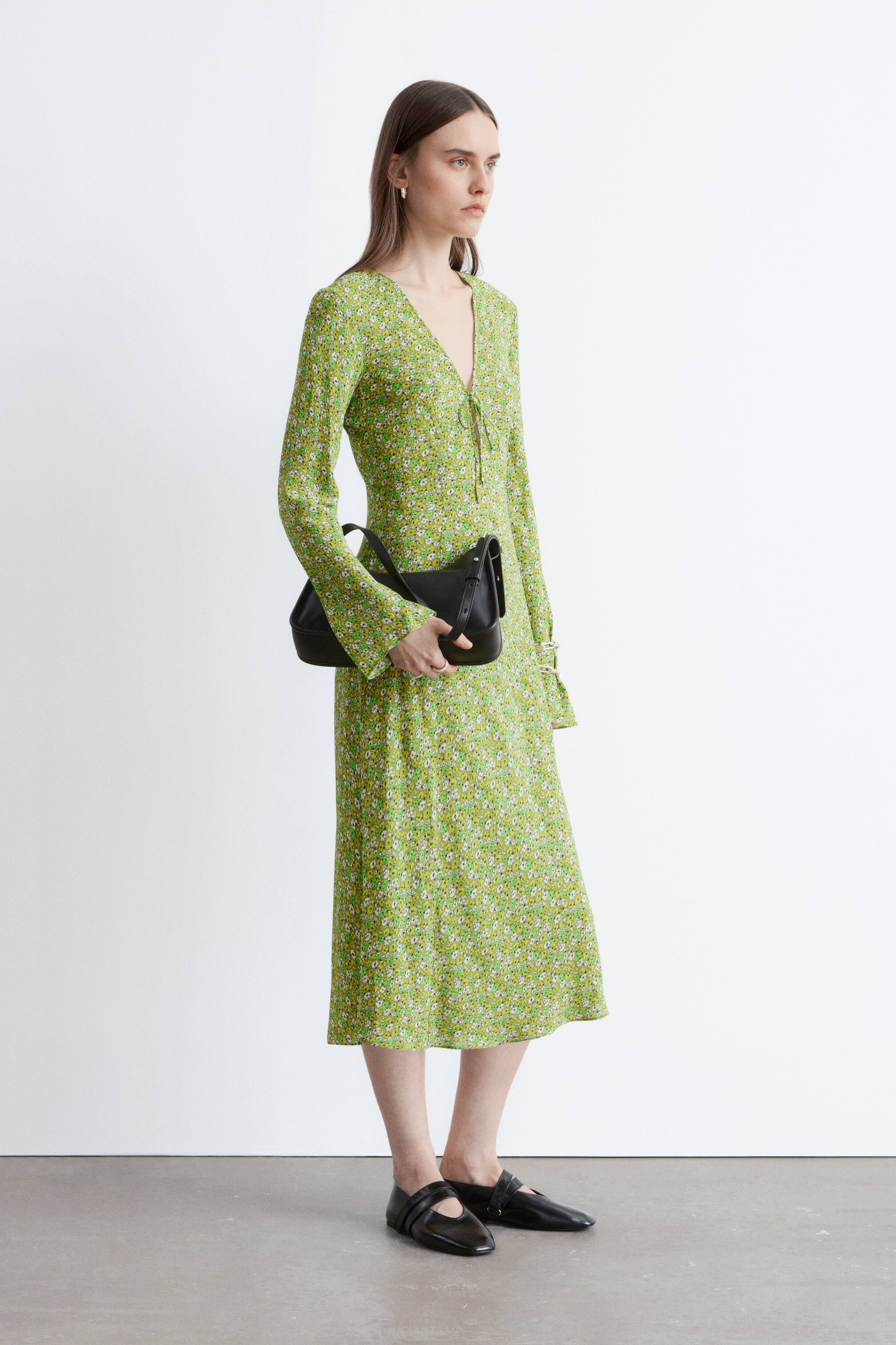 הצגת תמונה גדולה יותר: שמלת מידי פרחונית ירוקה מוצגת במבט צד. היא מתאפיינת במחשוף וי עם קשרים, שרוולים ארוכים ומותן מכווץ המוביל לחצאית מידי זורמת.