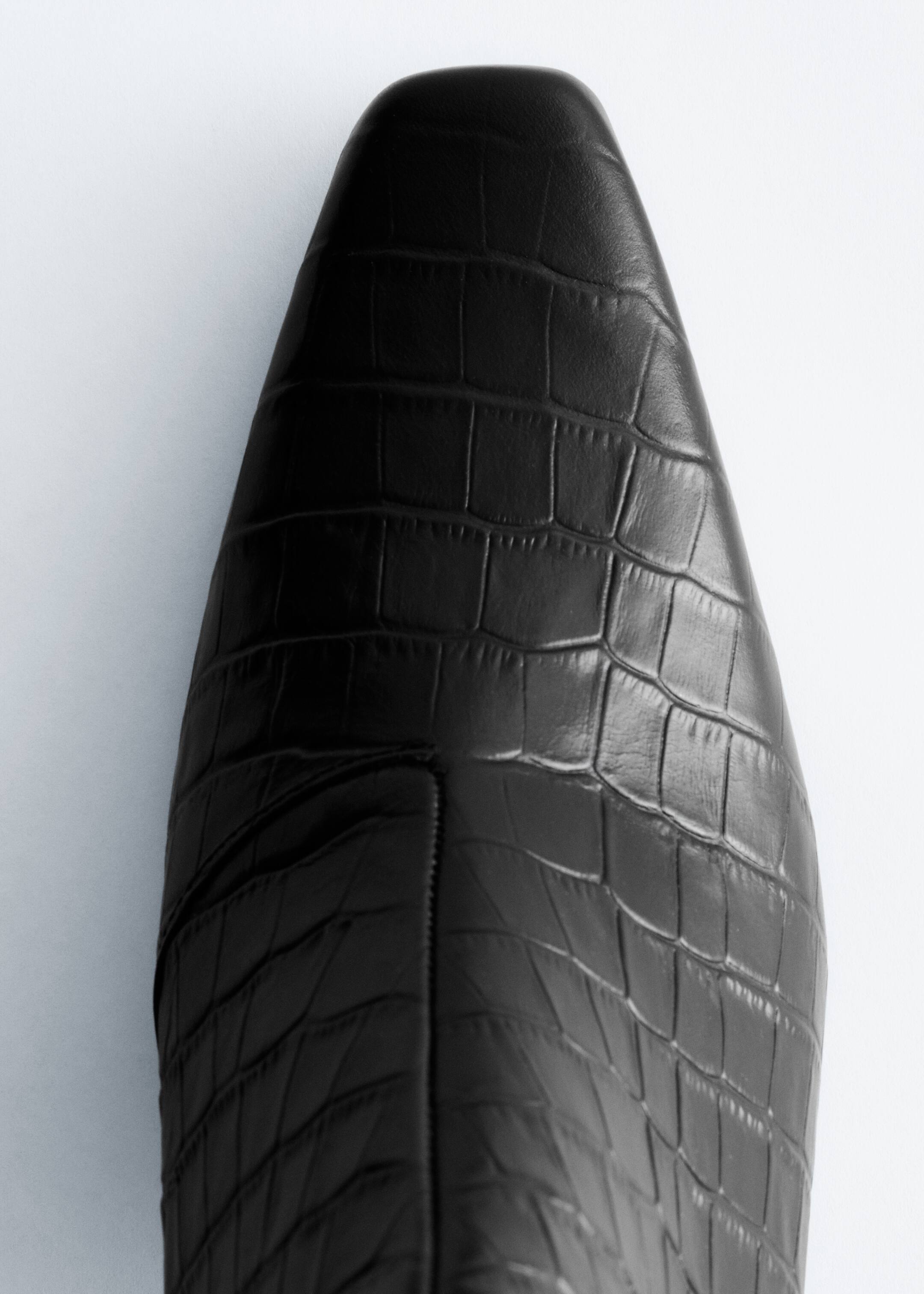 Ver imagen más grande: Se muestra la punta de una bota negra desde un ángulo cenital, que presenta una forma cuadrada suavizada y una textura en relieve con efecto de cocodrilo, con una costura central que recorre su empeine.