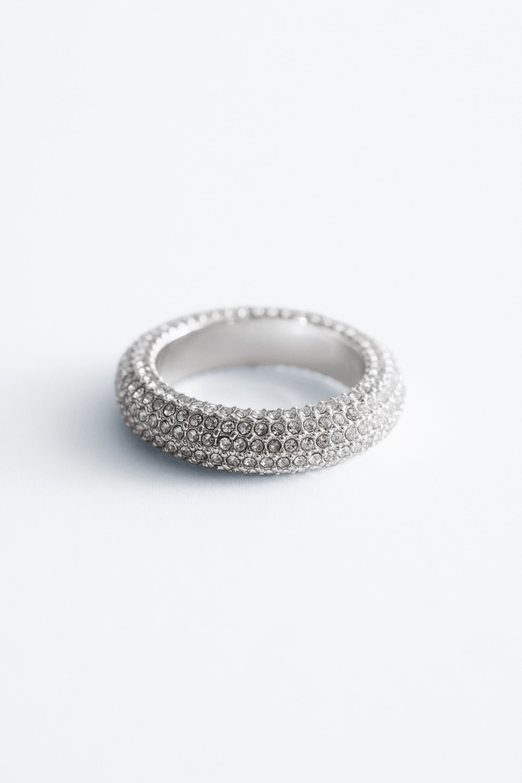 Visa större bild: En tjock ring är något vinklad och visar upp sin yta som är fullt dekorerad med många ljusreflekterande ädelstenar. Den inre ringen är synlig och verkar vara av ett polerat silverfärgat metall.