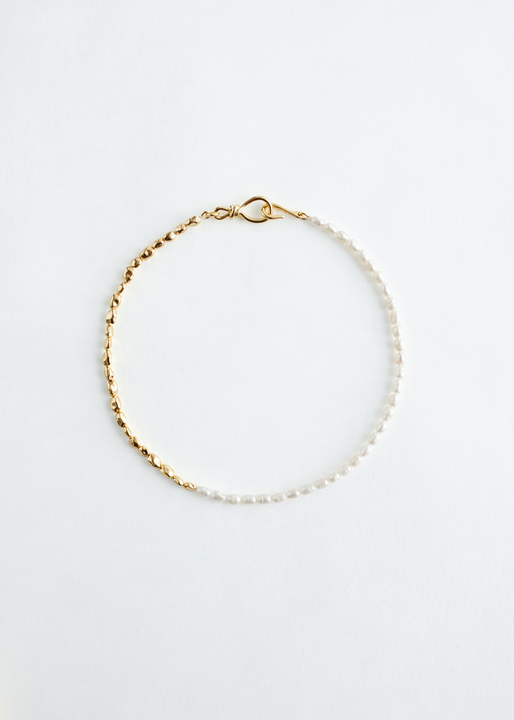 View larger image: A necklace is displayed flat, featuring a two-part design. One half is formed by irregular, gold-toned beads, and the other half is formed by irregular freshwater pearls. The necklace is fastening with a gold-toned wavy hook at one end and a wire loop knot at the other.