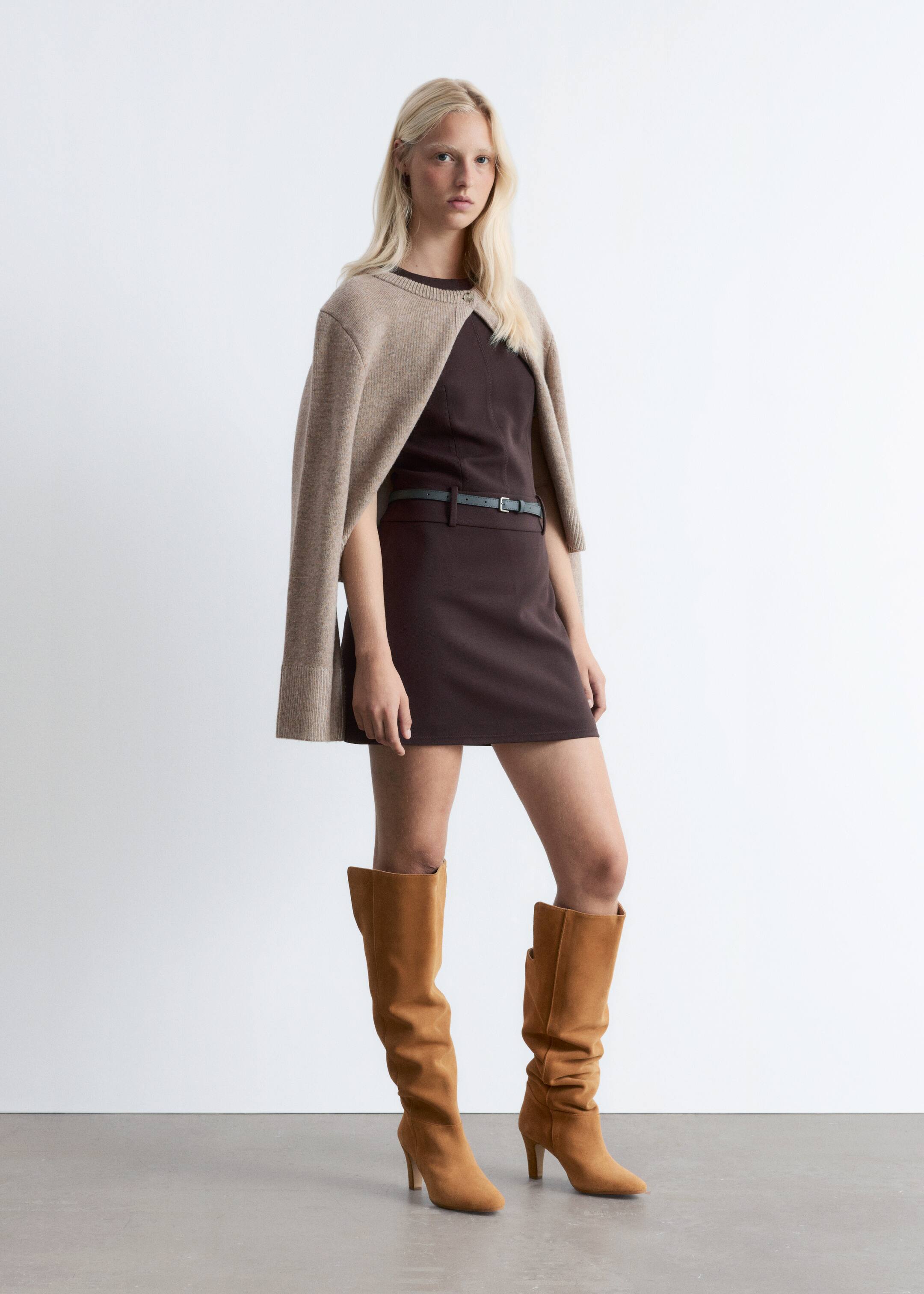 Visualizza immagine più grande: Stivali al ginocchio in camoscio color tan sono indossati dalla modella, caratterizzati da punte leggermente appuntite, tacchi rivestiti in camoscio e un gambale leggermente più largo intorno al polpaccio. Sono abbinati a un vestito marrone e un cardigan drappeggiato.