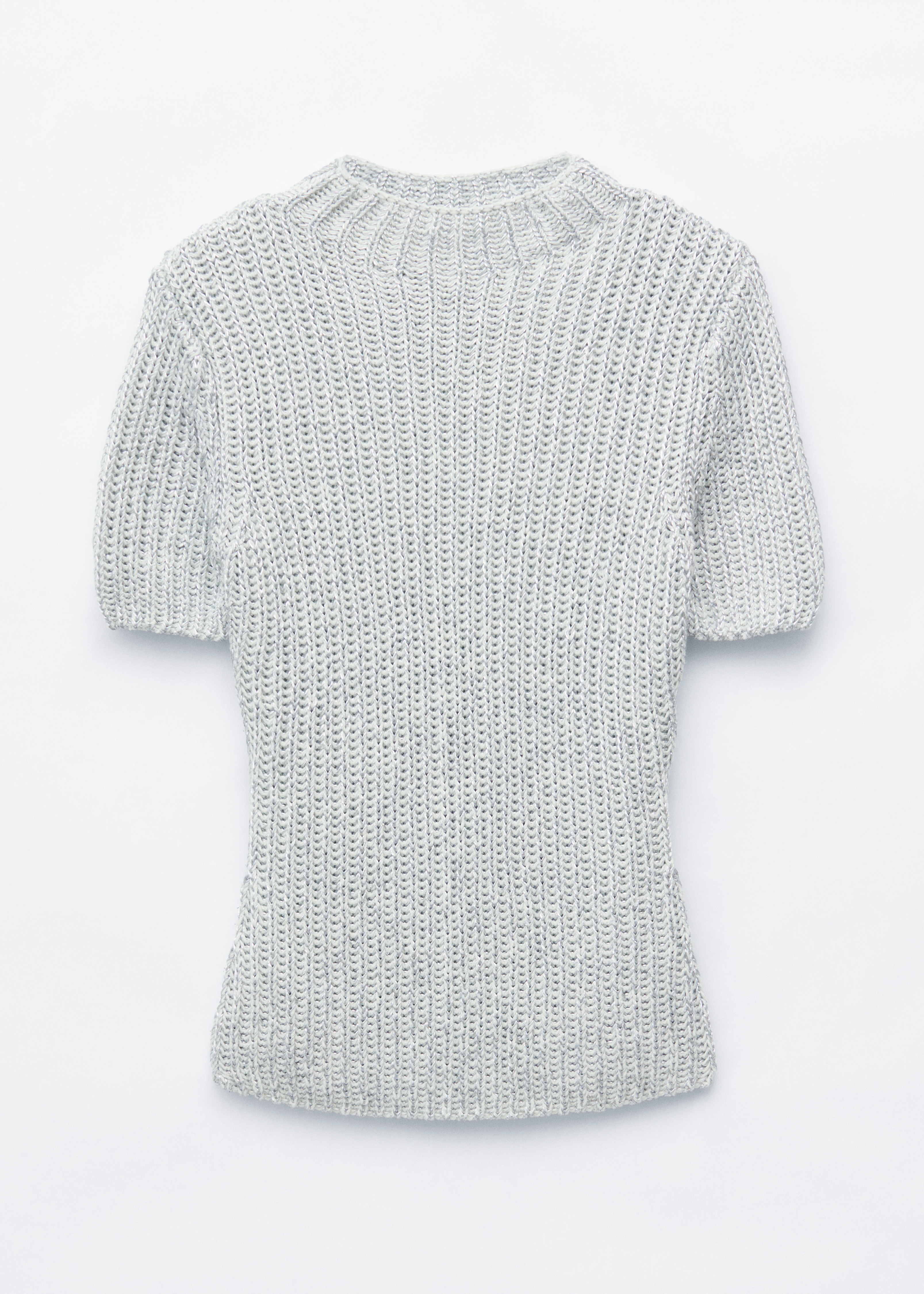 En stickad topp i metallisk look med en ljus silverfÃ¤rgad ribbad struktur, hÃ¶g rund halsringning och korta Ã¤rmar bÃ¤rs av modellen. Toppen stylas med en svart sammetskjol och en lila axelvÃ¤ska som bÃ¤rs Ã¶ver ena axeln.
