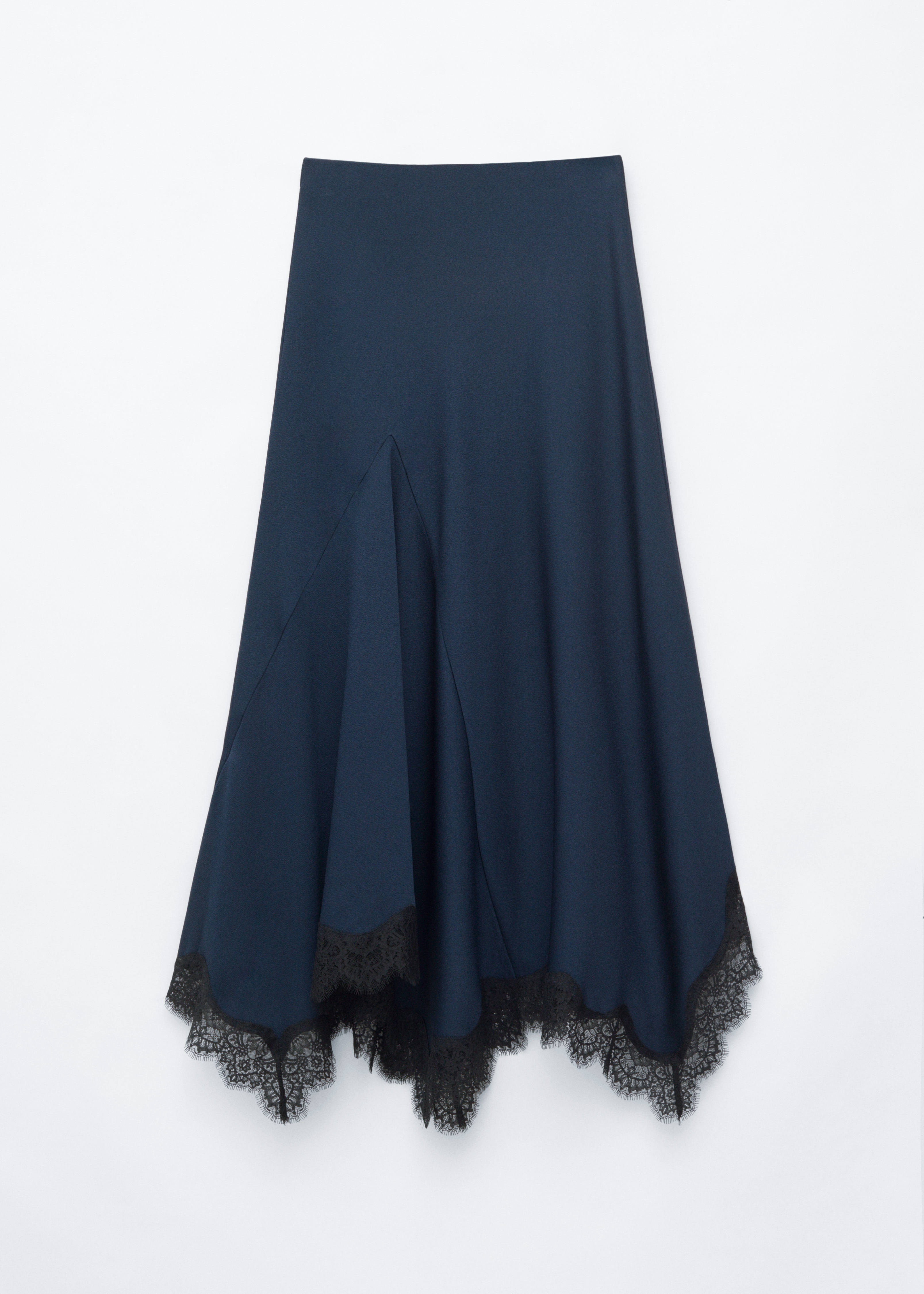 La modelo lleva una falda acampanada azul oscuro con bajo asimÃ©trico rematado con delicado encaje negro. La prenda se combina con una blusa plisada de manga larga en azul oscuro a juego, unos zapatos de tacÃ³n slingback negros y un bolso tote negro de tejido trenzado.