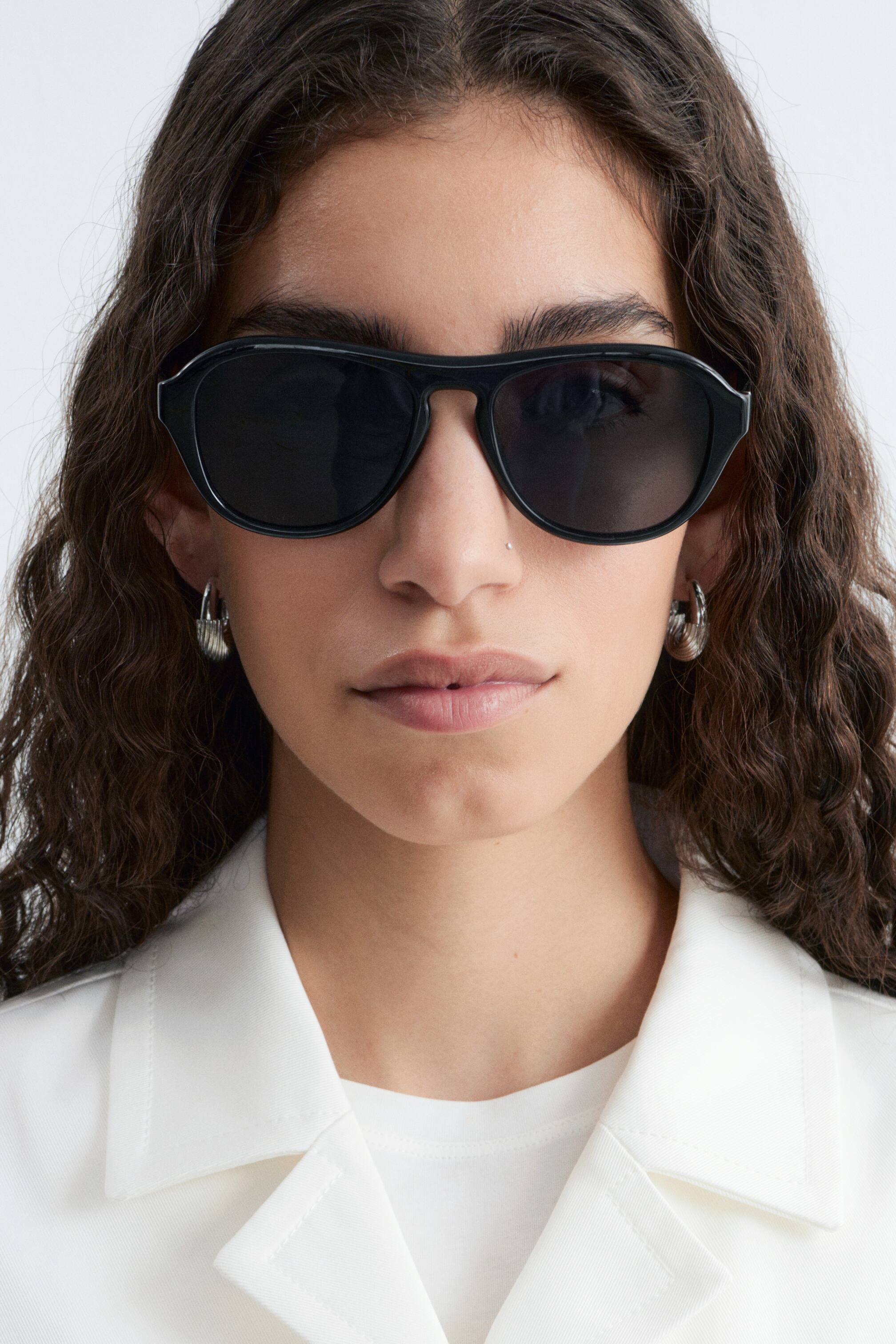 View larger image: Black sunglasses are being worn, featuring dark tinted lenses and a thick, full-rim frame with a prominent flat top bar.