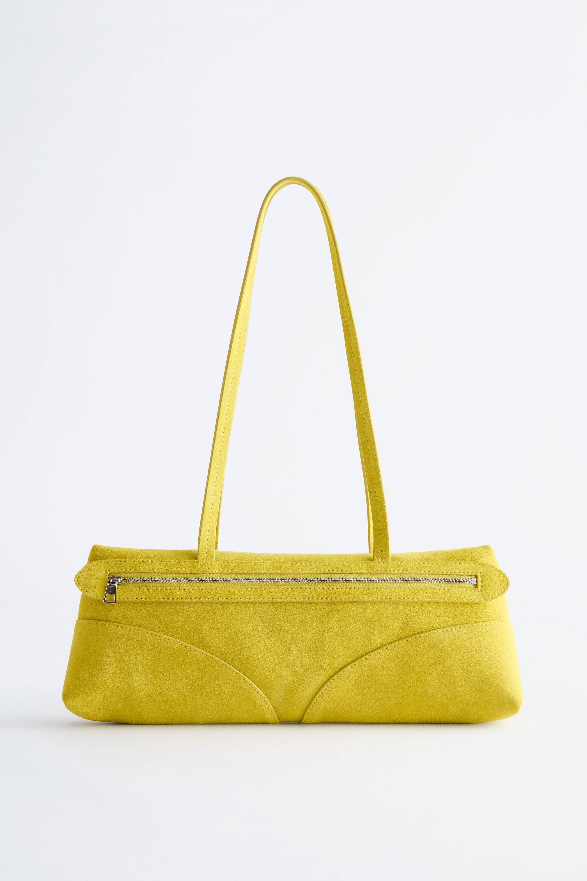 View larger image: A yellow suede-like shoulder bag is presented FRONT, featuring an elongated rectangular silhouette. It is displaying a silver-toned zip closure along the top and two slender straps, with curved stitched panels detailing its front surface.