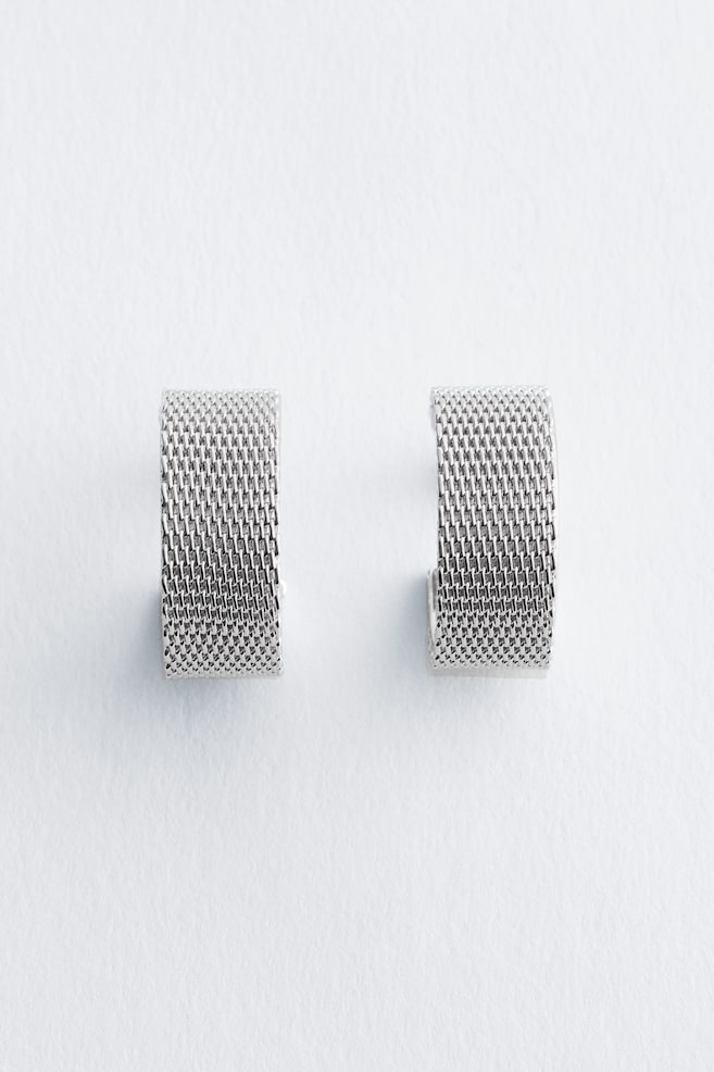 A pair of wide, silver-toned, C-shaped earrings featuring a fine mesh texture, presented from the front. - 1