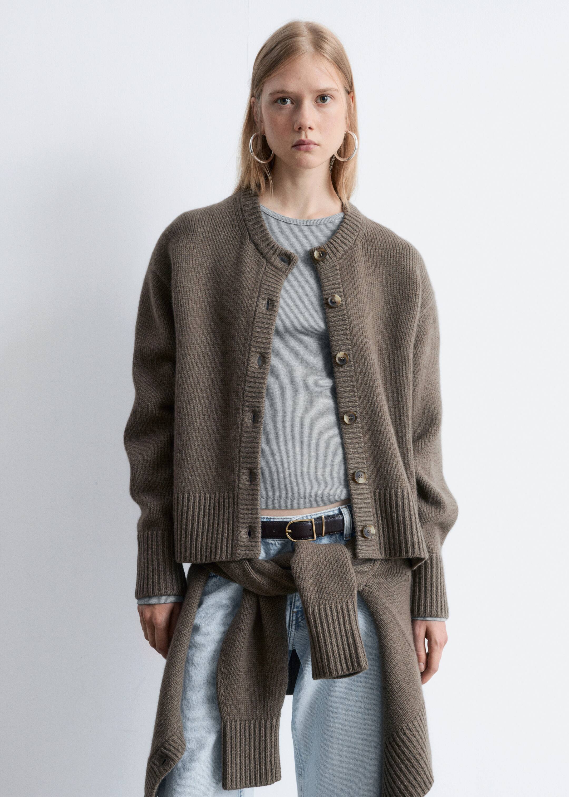 Agrandir l'image: Un cardigan en tricot brun fait face à l'avant, avec un col rond, une fermeture à boutons avec des boutons brun foncé, et des poignets et un ourlet côtelés. Il est superposé à un haut côtelé gris clair, tandis qu'un vêtement en tricot brun similaire est stylé autour de la taille.