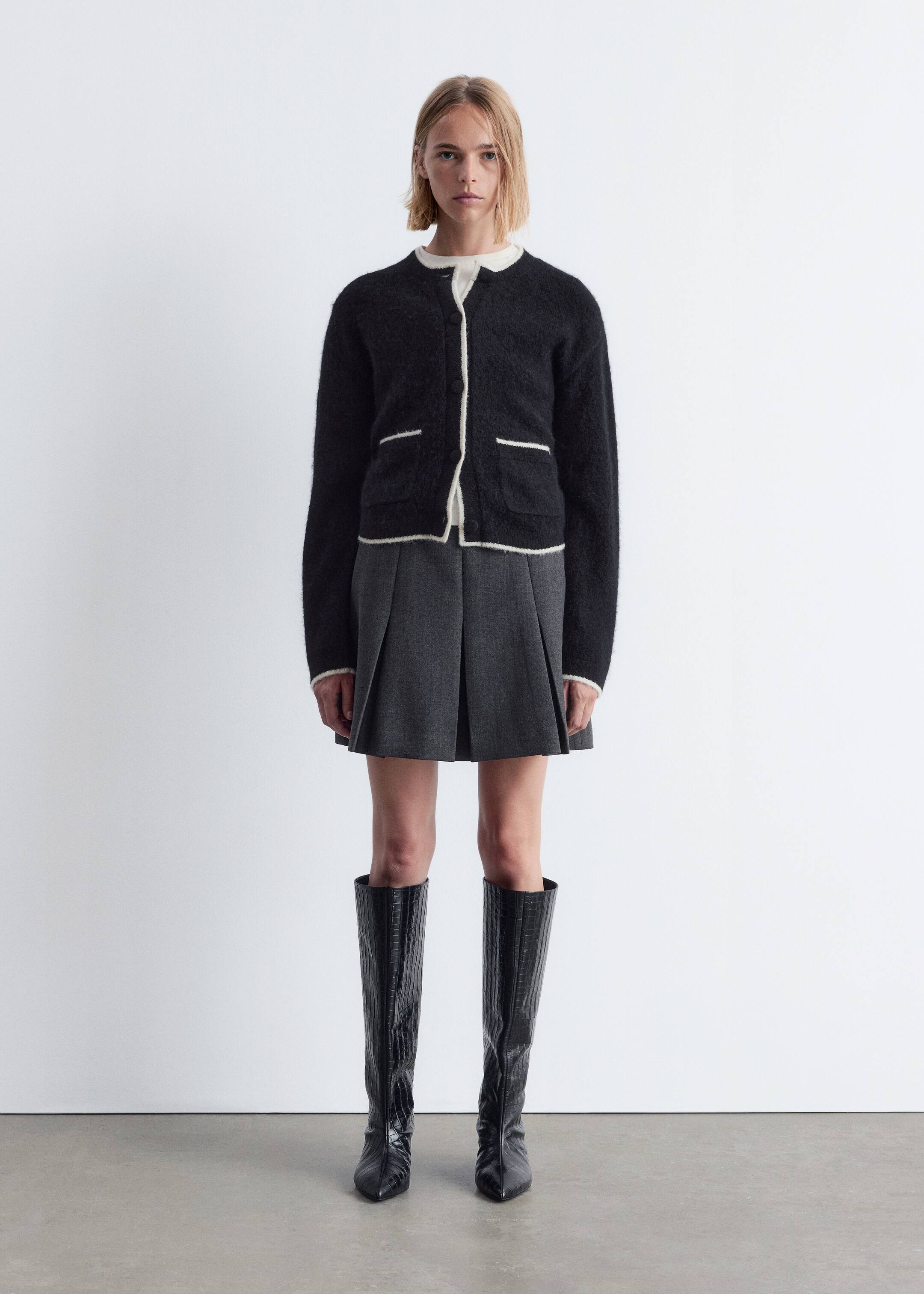 Agrandir l'image: Un cardigan noir est présenté de face. Il présente une texture tricotée duveteuse avec des détails de passepoil blanc le long de l'encolure ronde, de la patte de boutonnage, de l'ourlet et des deux poches plaquées avant. Le cardigan est porté sur un haut blanc, avec son encolure et ses poignets visiblement superposés en dessous.