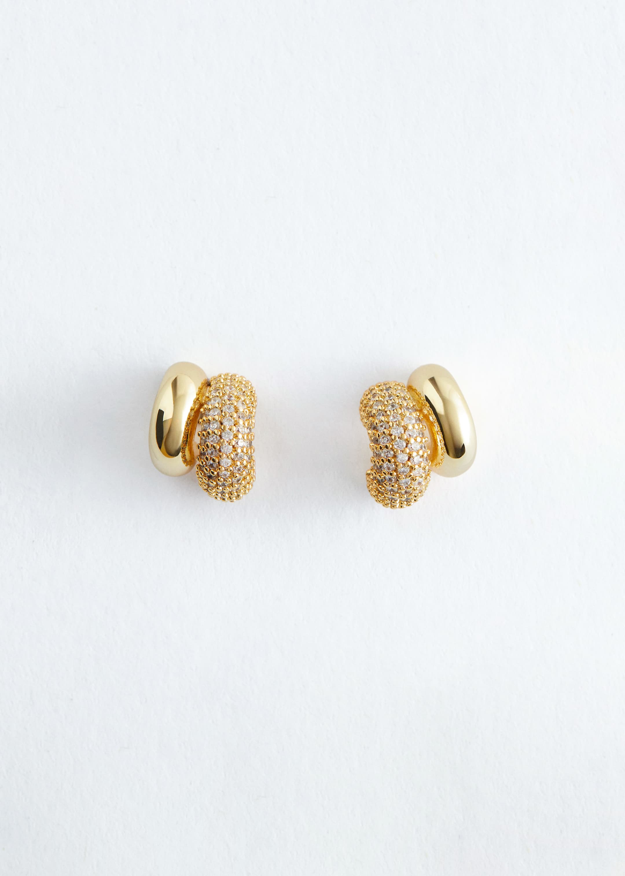 Ver imagen más grande: Un par de pendientes en tono dorado presenta un diseño con un elemento en forma de C liso y pulido junto a un elemento en forma de C con pavé, este último intrincadamente adornado con piedras claras.