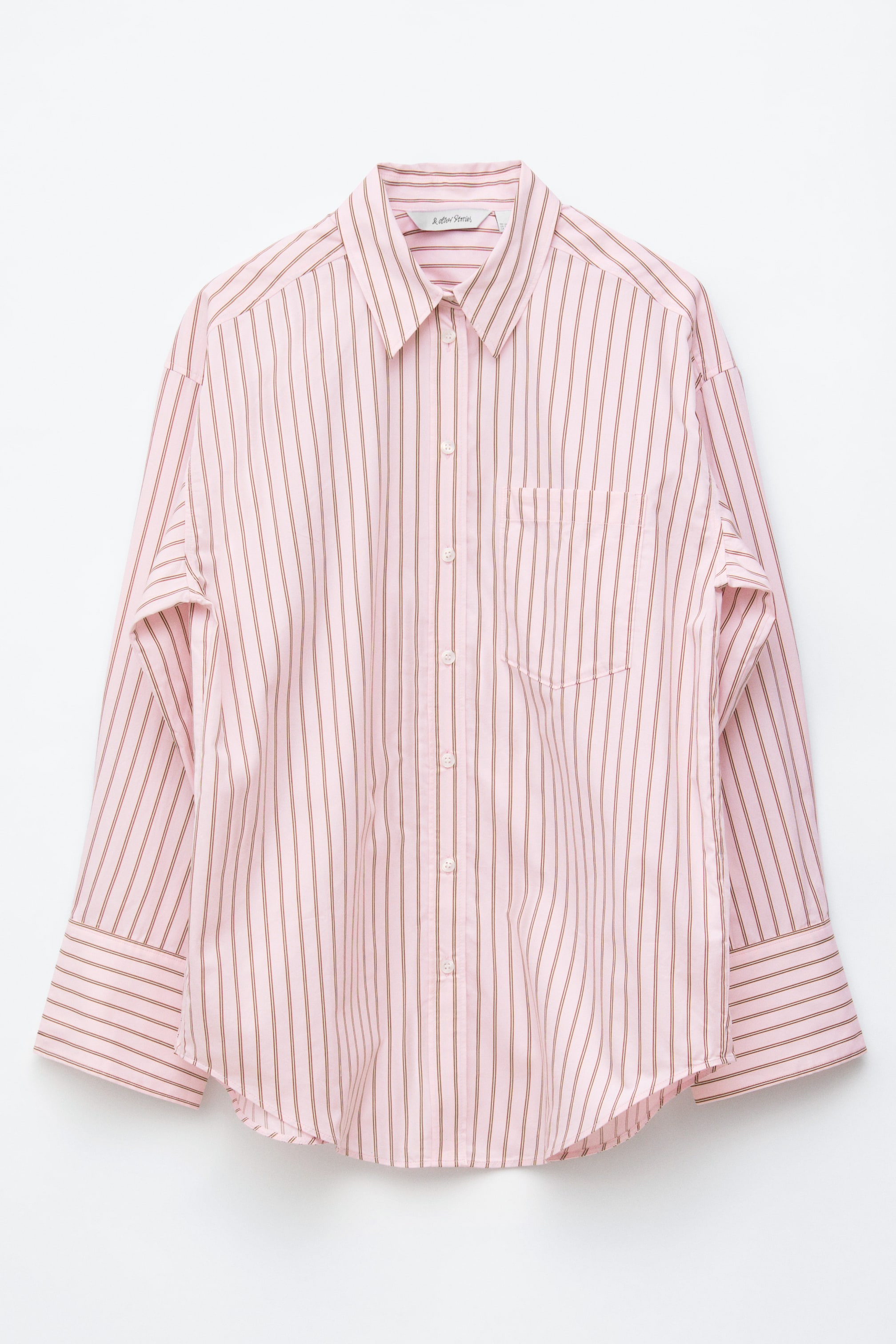 Grotere afbeelding bekijken: Een roze hemd met verticale bruine strepen wordt van de VOORKANT getoond. Het heeft een losse pasvorm, een puntige kraag en een knoopsluiting aan de voorkant met tonale knopen. Lange mouwen reiken tot aan de geknoopte manchetten, en een opgestikte zak bevindt zich op de linkerborst, met doorstikte naden die de constructie benadrukken.