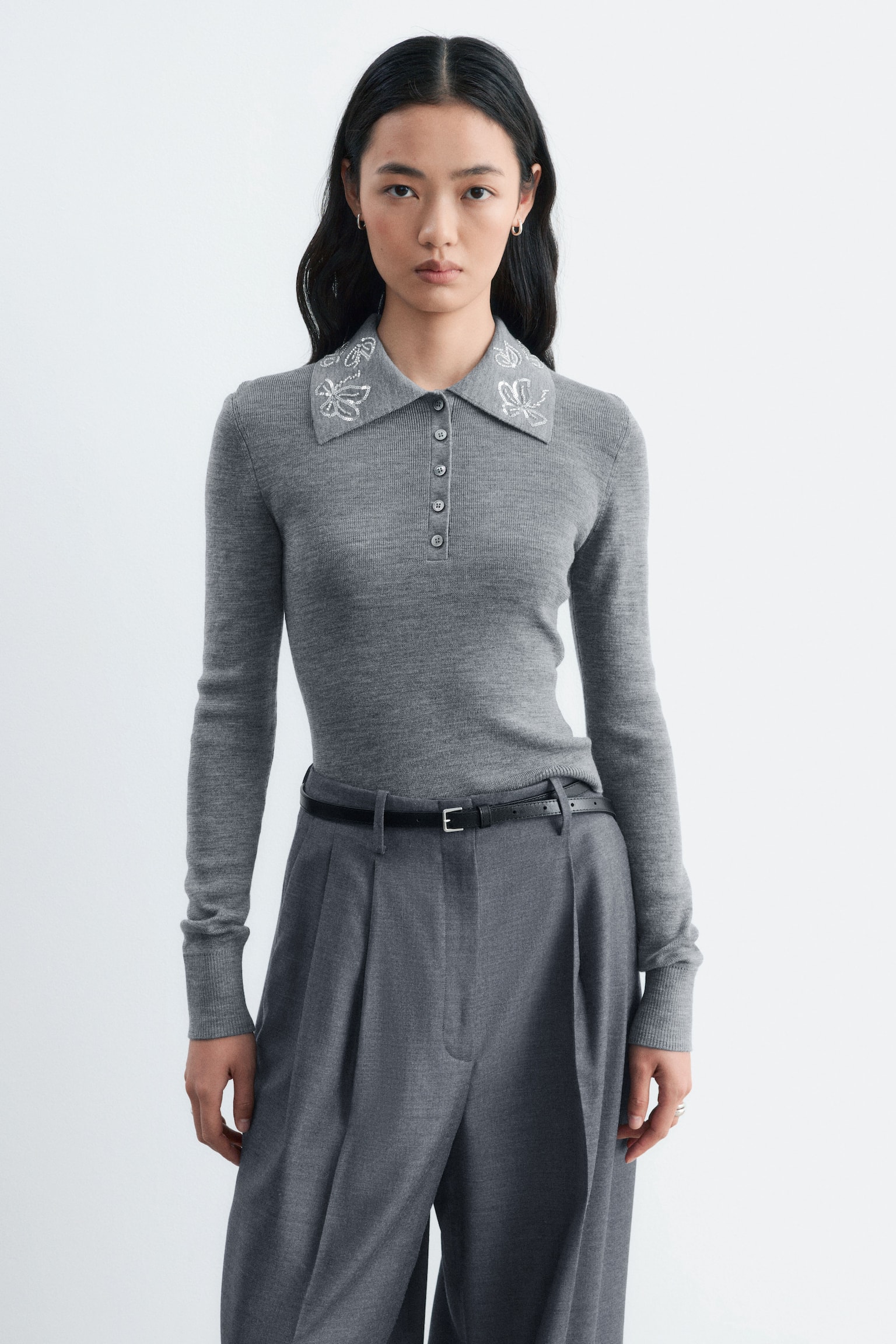 En grå uld-pullover med polokrave vises forfra i en slim-fit pasform og fremhæver en spids krave pyntet med sommerfuglebroderi med sølvpailletter. Pulloveren har en knaplukning med fem knapper langs brystet samt lange ærmer med ribkanter. - 1