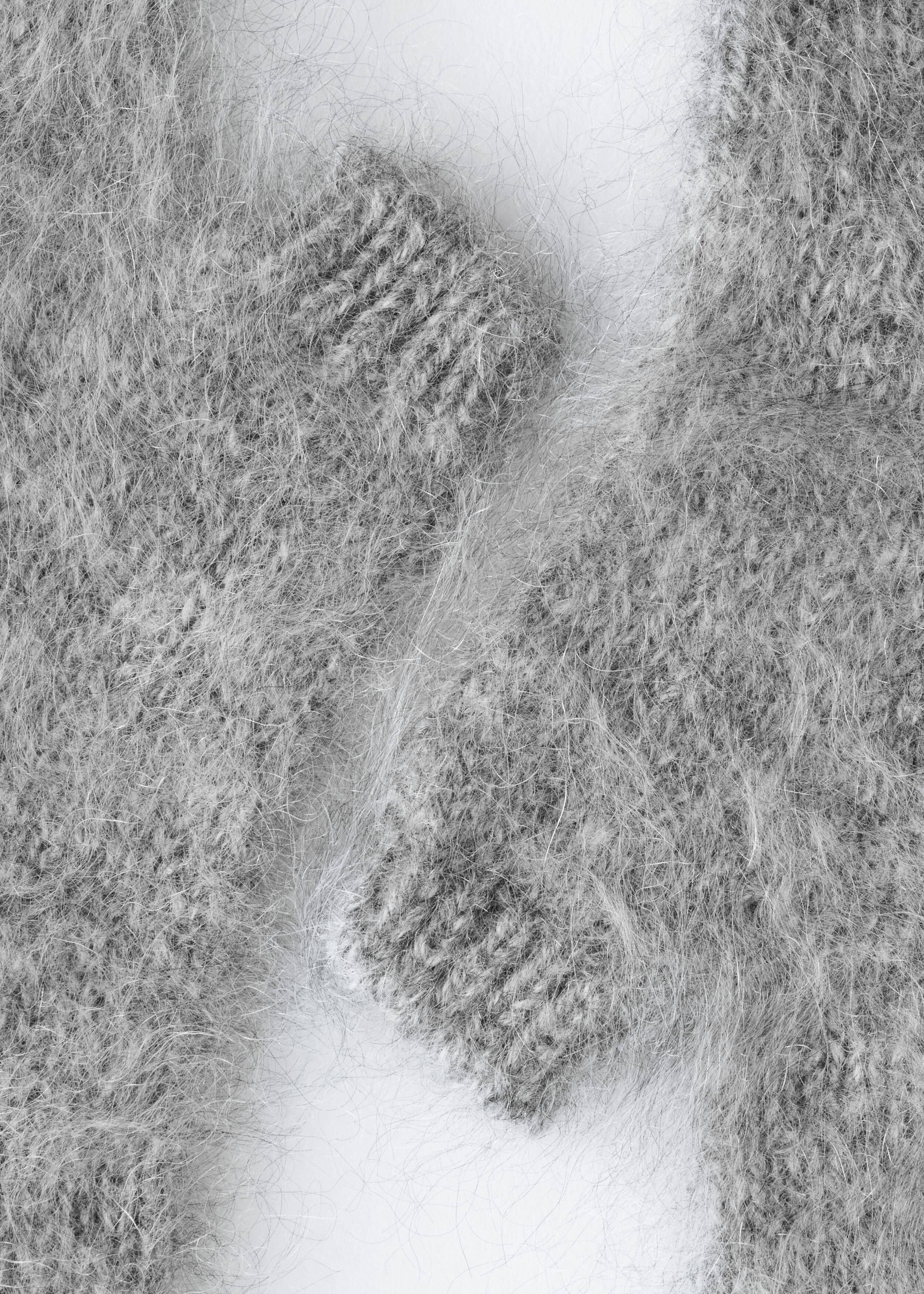 Grey fingerless gloves show a heavily brushed, fuzzy cashmere texture with soft, long fibers. This close-up highlights the ribbed cuffs at the openings and the knit construction beneath the brushed finish.