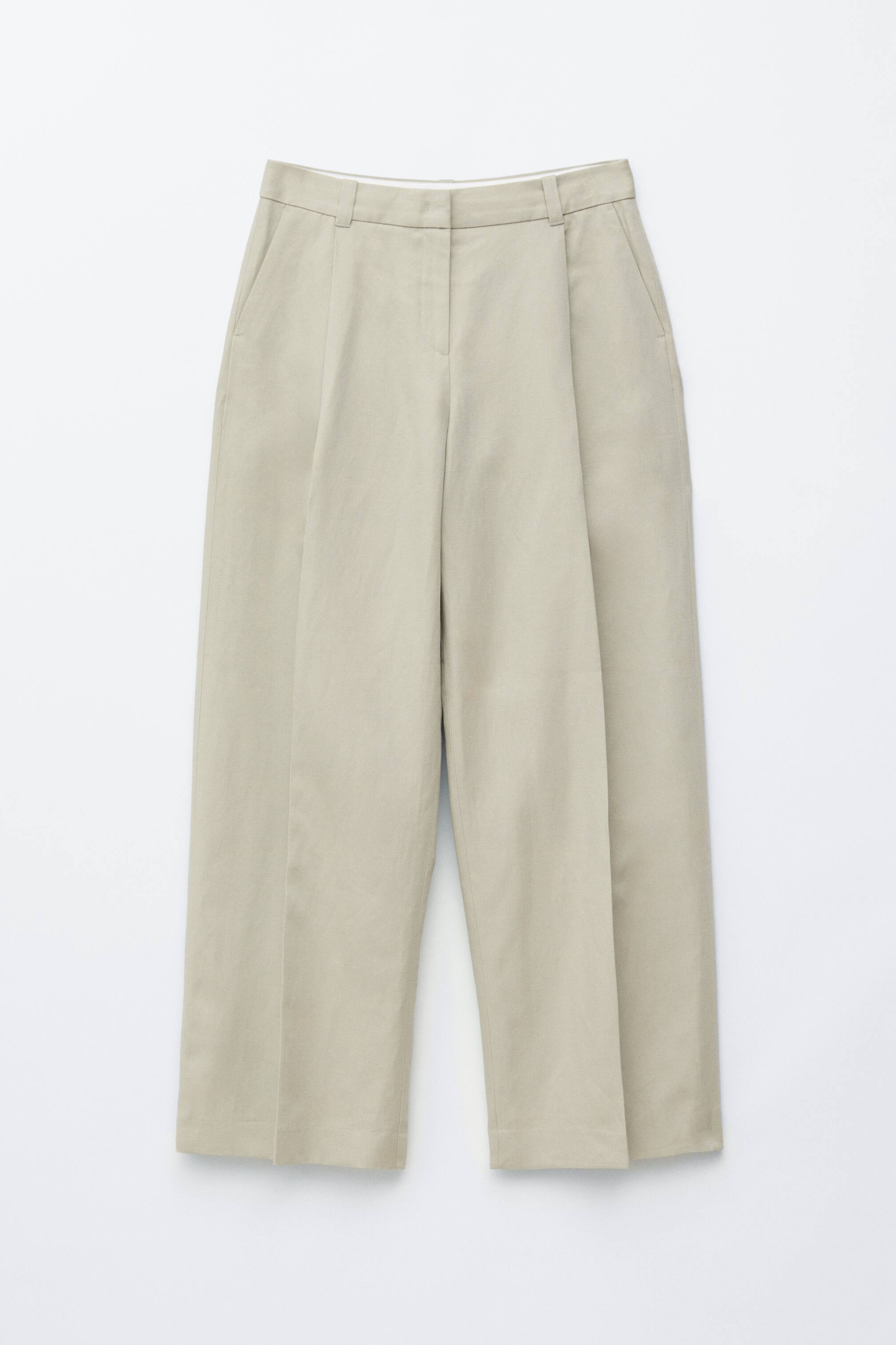 Zobrazit větší obrázek: Světle béžové kalhoty jsou zobrazeny zepředu, ukazují uvolněnou siluetu s jediným předním záhybem, lisovanými sklady po celé délce nohavic a šikmými bočními kapsami.