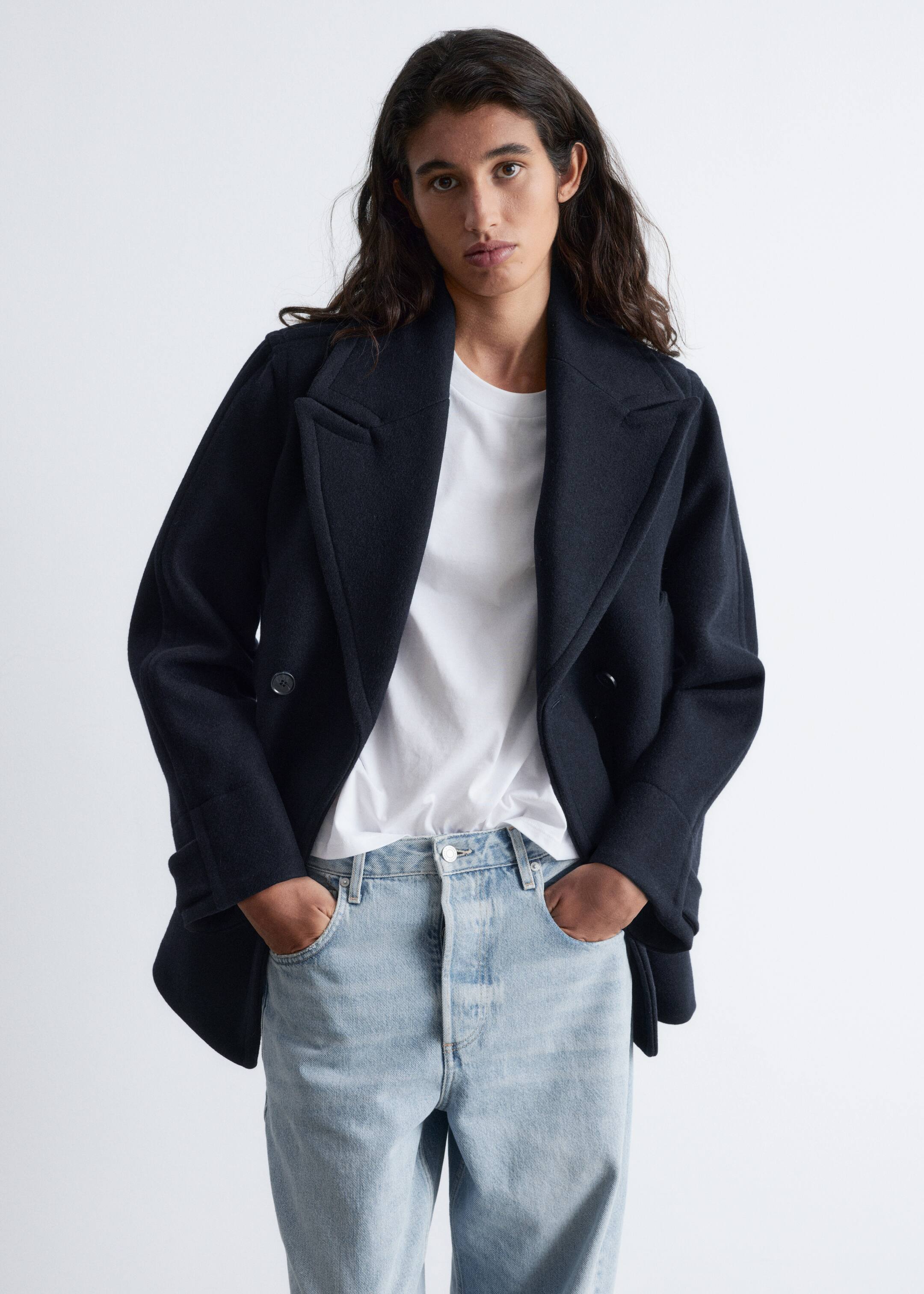 Größeres Bild anzeigen: Ein dunkler, zweireihiger Caban mit breiten Revers wird vom Model getragen. Das Model steht mit den Händen in den Manteltaschen, der über einem weißen T-Shirt und hell gewaschenen Jeans gestylt ist.