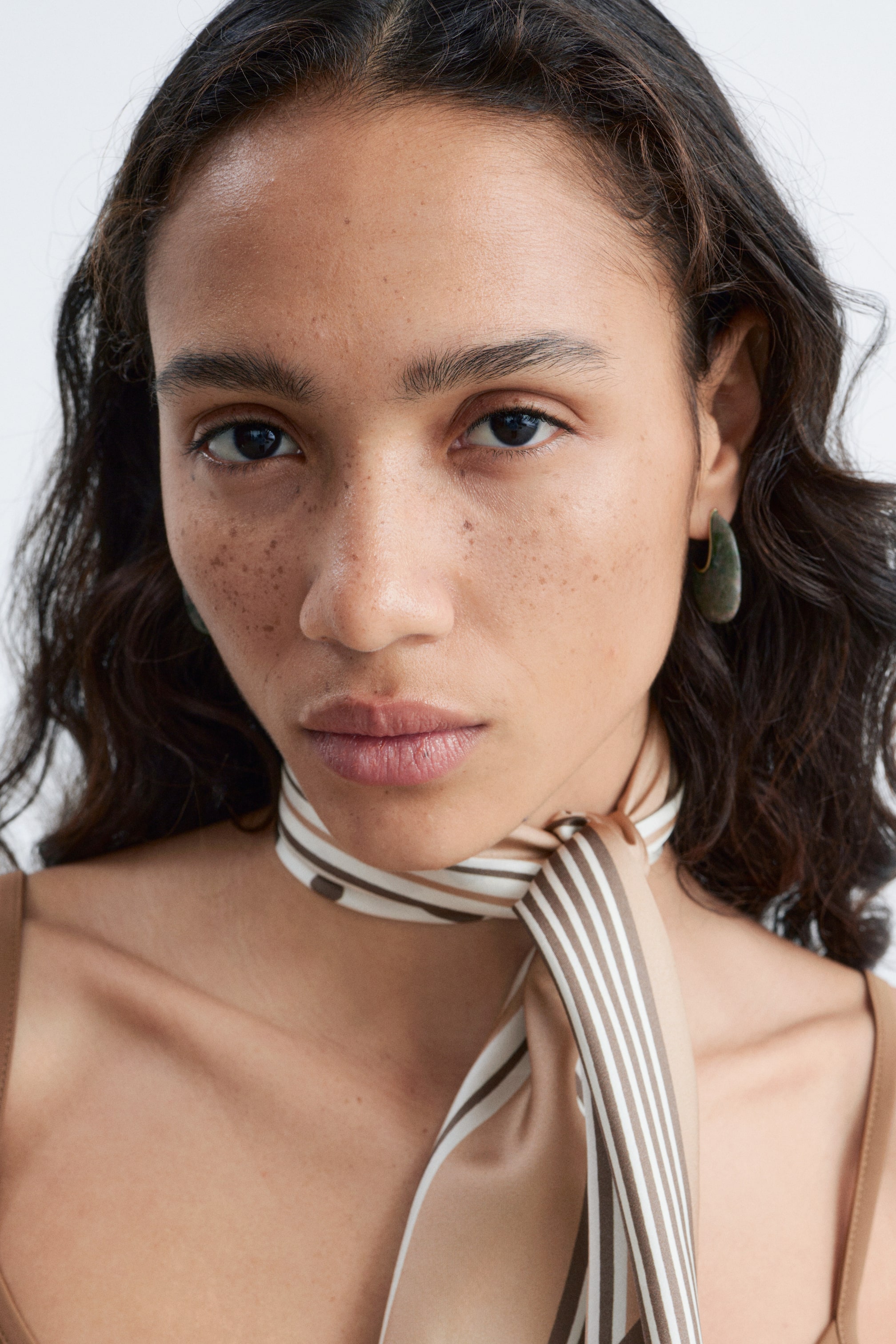 Agrandir l'image: Un foulard est noué autour du cou, arborant un motif de rayures alternées beige, blanc et marron.