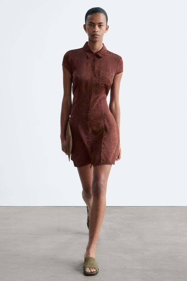 A textured brown shirt dress is facing forward, featuring a pointed collar, short sleeves, a full button-front placket, and a single patch pocket on the left chest. It is displaying a fitted silhouette that ends above the knee. - 1