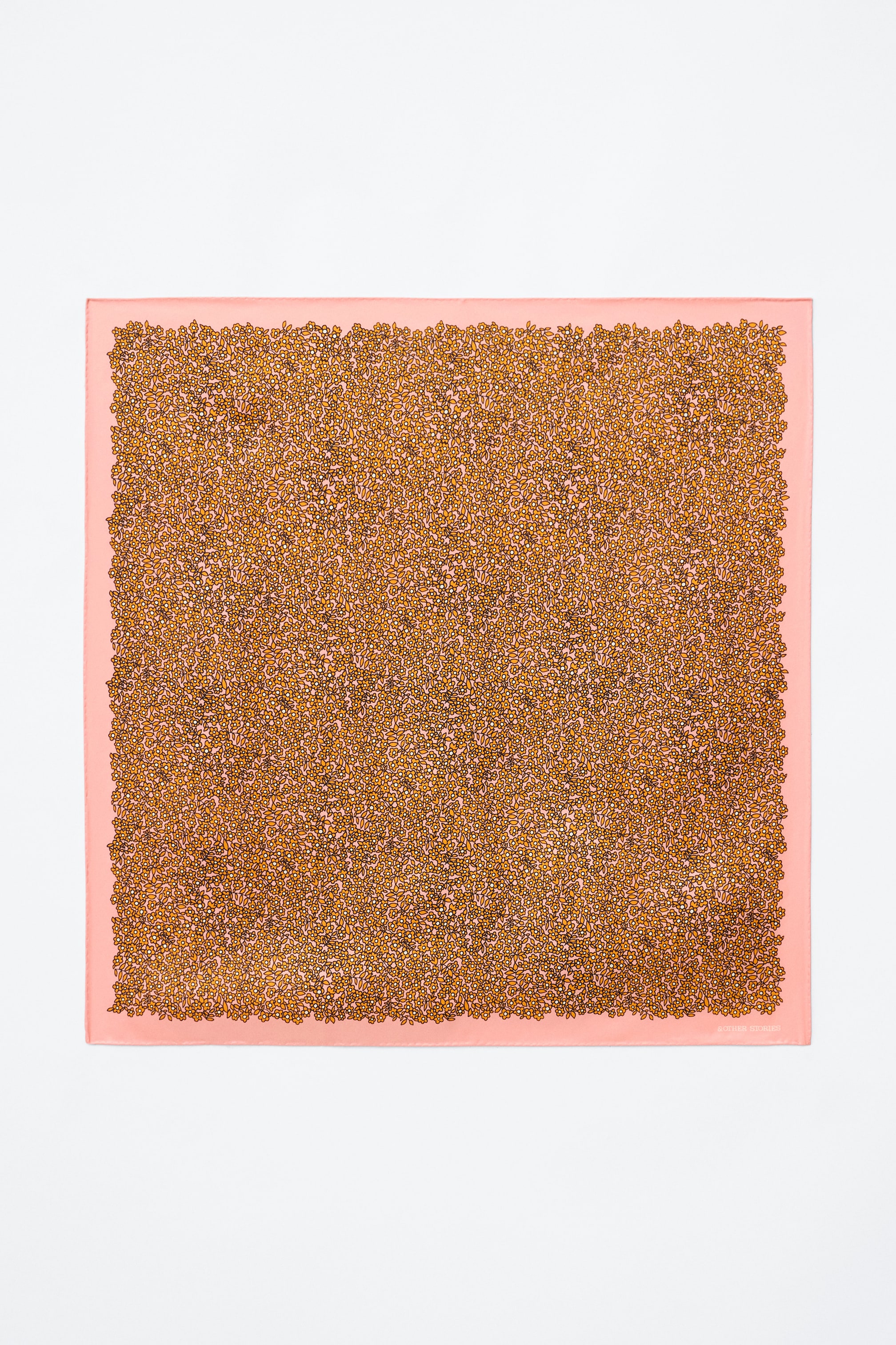 Visualizza l'immagine ingrandita: Un foulard quadrato è disteso piatto, mostrando un motivo denso di piccole forme floreali color oro-arancio con contorni scuri su uno sfondo rosa chiaro, incorniciato da un bordo solido rosa chiaro.