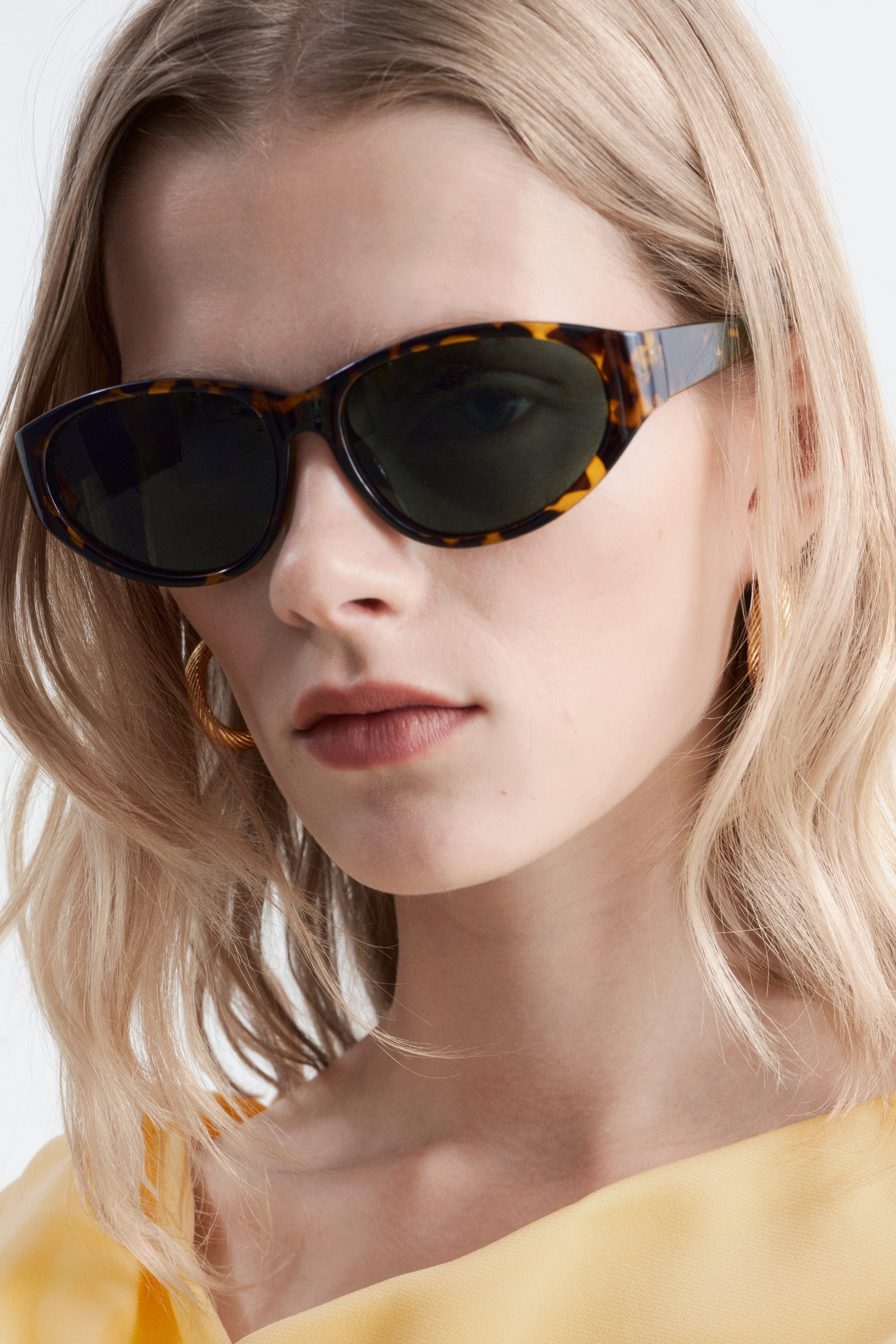 Größeres Bild ansehen: Die Schildpatt-Katzenaugen-Sonnenbrille mit dunkel getönten ovalen Gläsern wird vom Model getragen.