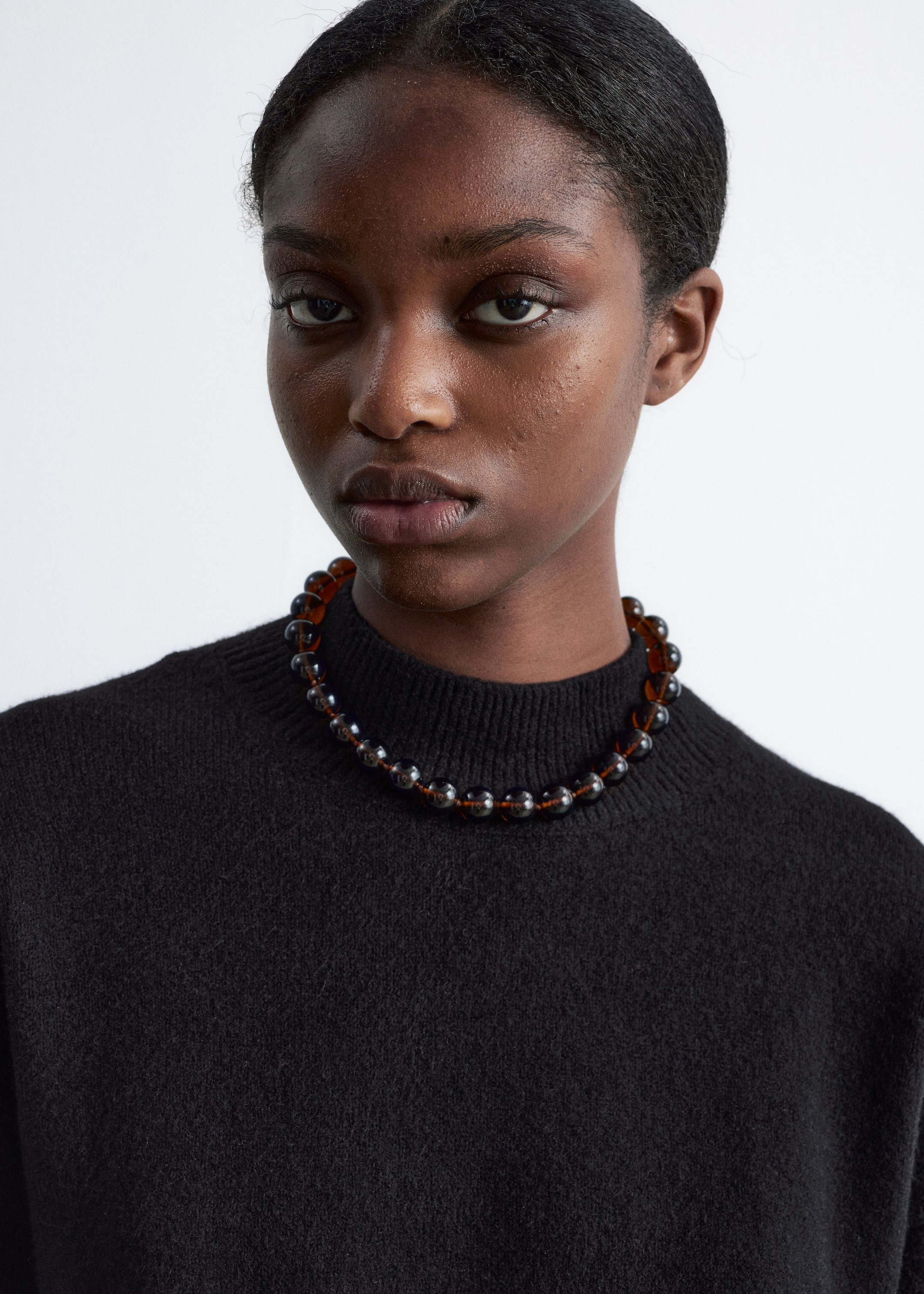 Visa större bild: Ett halsband i choker-stil har stora, runda, genomskinliga bruna och mörkgrå pärlor som är trädda på en tunn, synlig tråd. Halsbandet vilar precis ovanför nyckelbenet och bärs över en svart polotröja.
