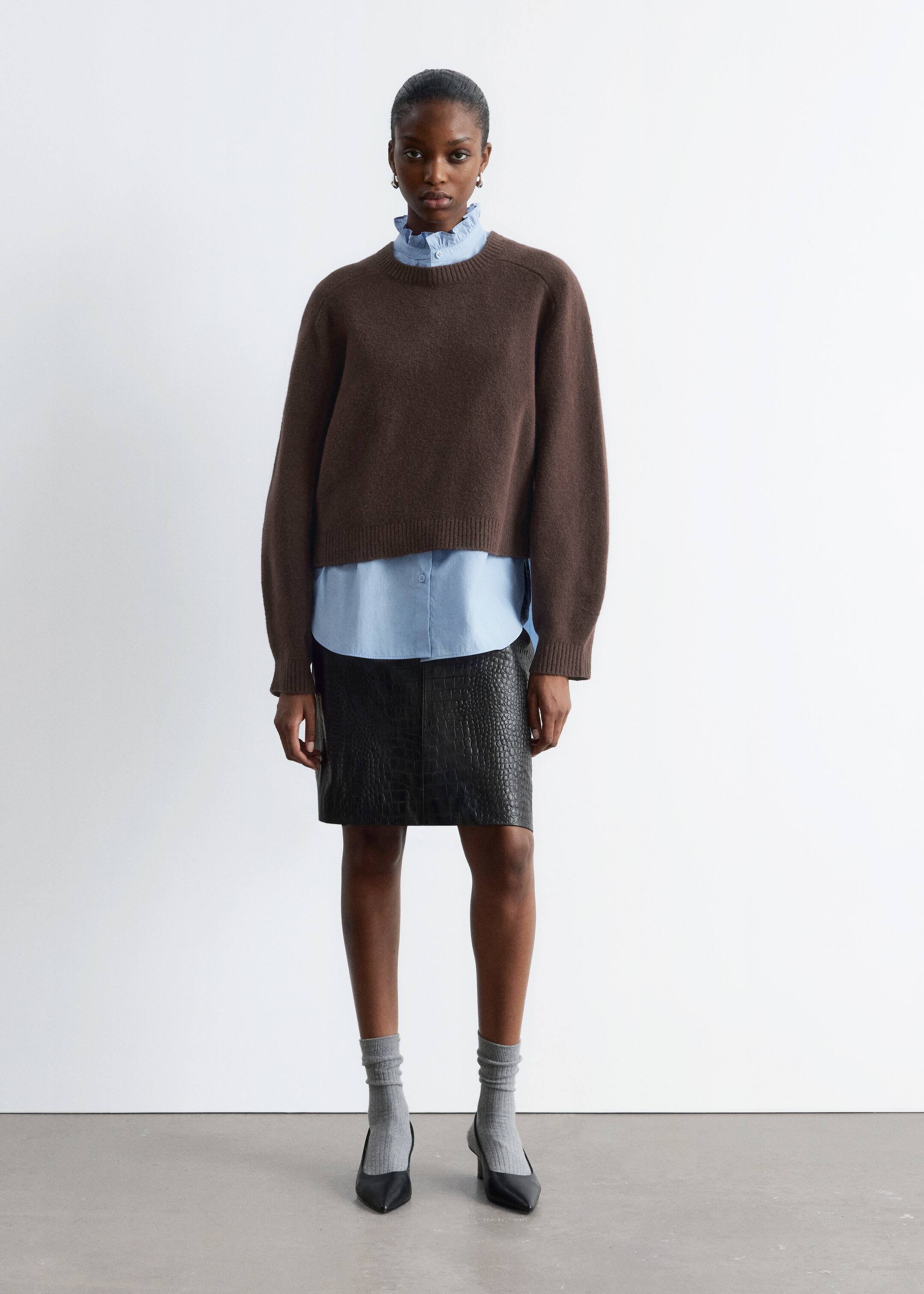 Grösseres Bild ansehen: Ein brauner Pullover mit Rundhalsausschnitt wird getragen, nach vorne gerichtet, mit einer entspannten Passform und langen Raglanärmeln. Er präsentiert eine verkürzte Länge mit gerippten Bündchen und einem gerippten Saum und ist über einem hellblauen Hemd mit Kragen geschichtet.