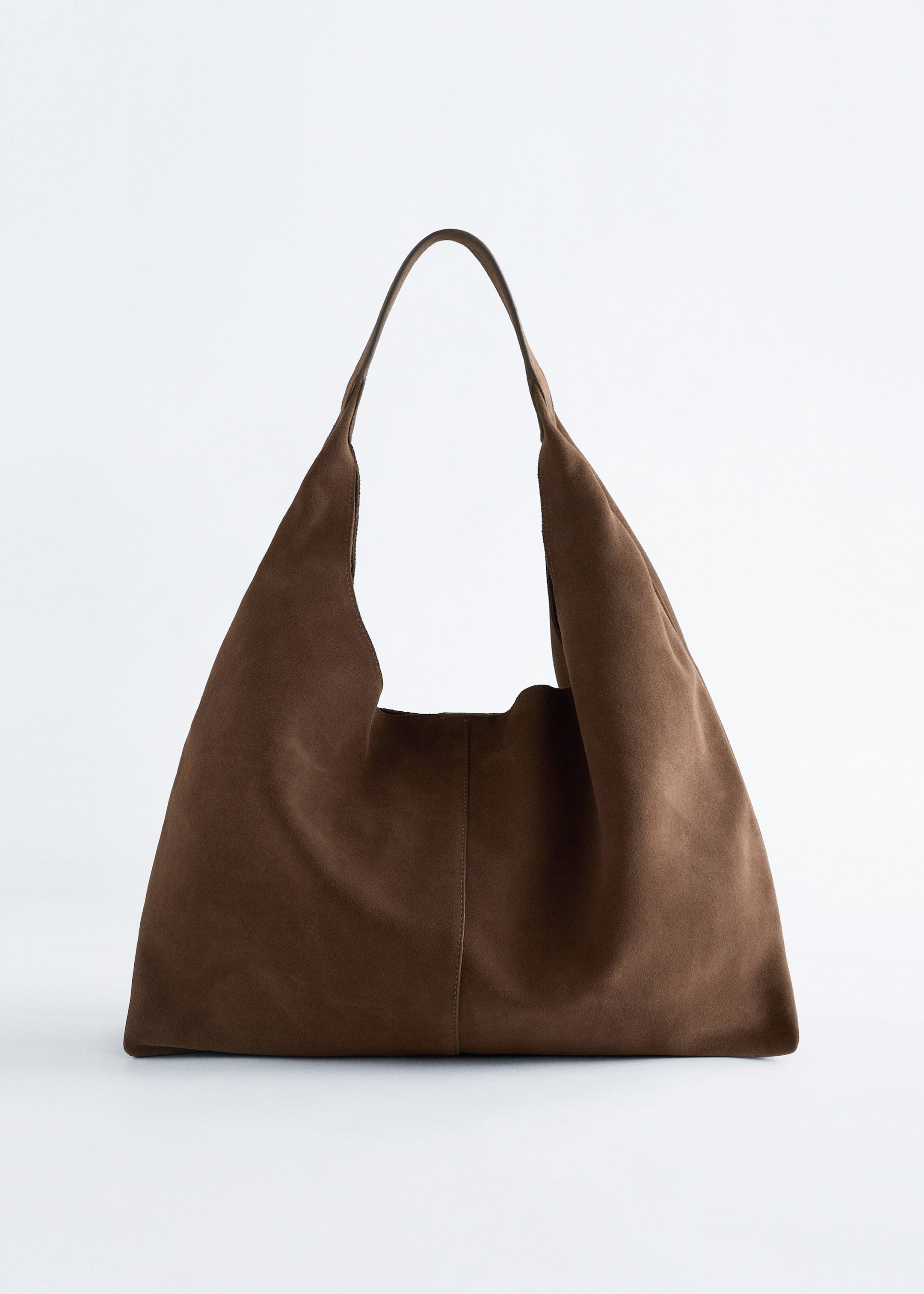 Visualizza immagine più grande: Una borsa tote in camoscio marrone è mostrata dal davanti, con una finitura opaca e una cucitura decorativa verticale prominente lungo il centro, con il suo corpo morbido e cascante che forma una curva continua con il manico integrato.