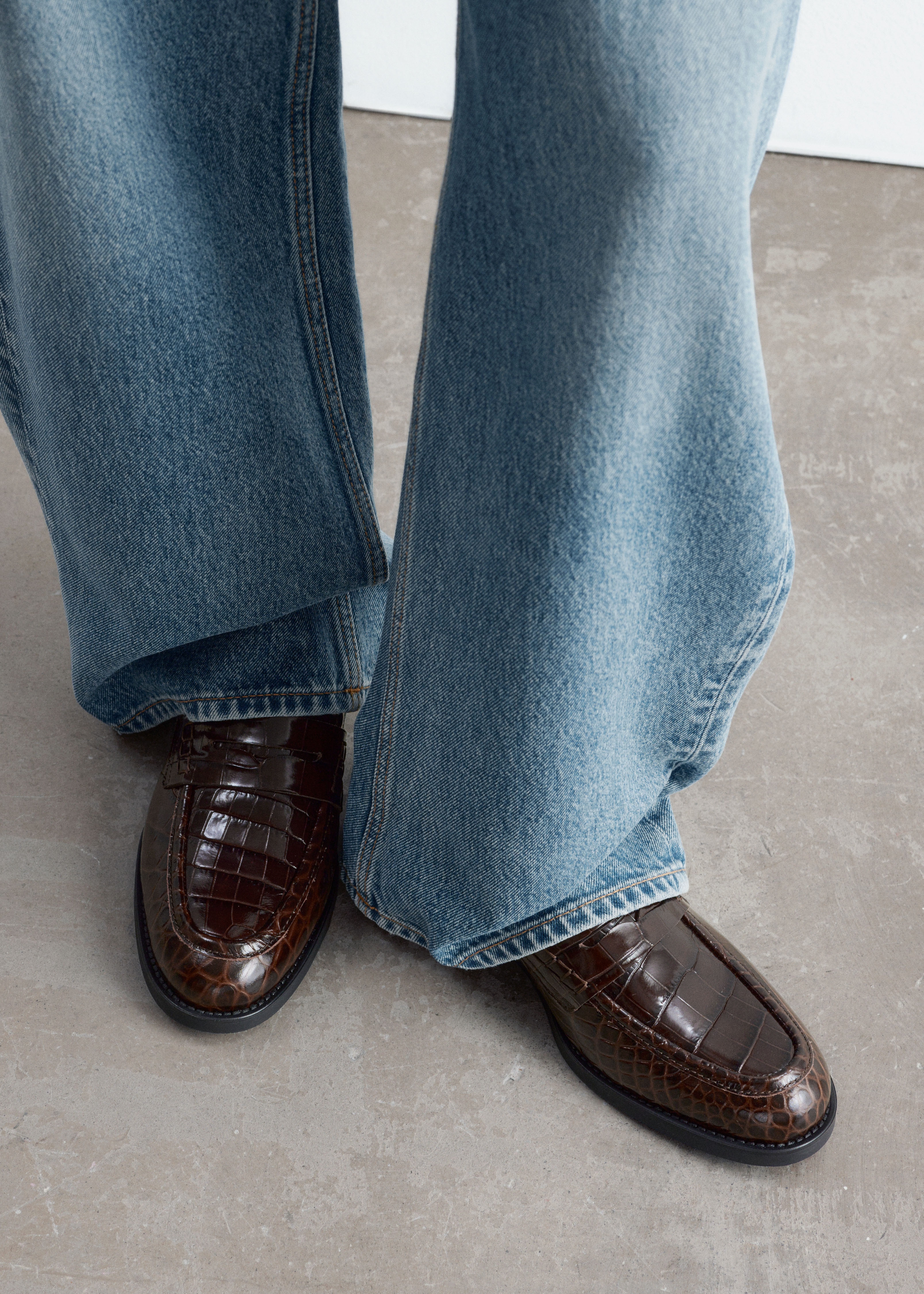 Un mocasin penny clasic, din piele maro cu finisaj lucios Èi imprimeu embosat crocodil, este prezentat din profil lateral. Pantoful evidenÈiazÄ cusÄturi decorative Ã®n jurul vÃ¢rfului, o baretÄ tradiÈionalÄ penny peste vÃ¢rf Èi o talpÄ groasÄ din cauciuc negru.