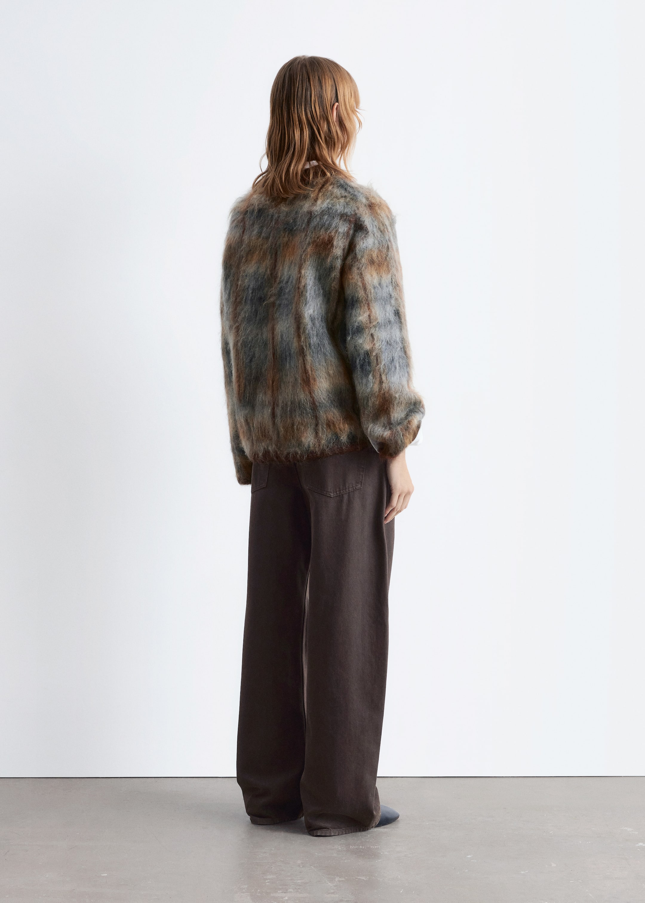 Größeres Bild anzeigen: Ein langärmeliger Pullover mit einer melierten braunen, grauen und blauen flauschigen Textur wird vom Model getragen. Er zeigt eine lockere Passform und wird mit dunklen, weit geschnittenen Hosen gestylt, während das Model mit dem Rücken zum Betrachter steht.