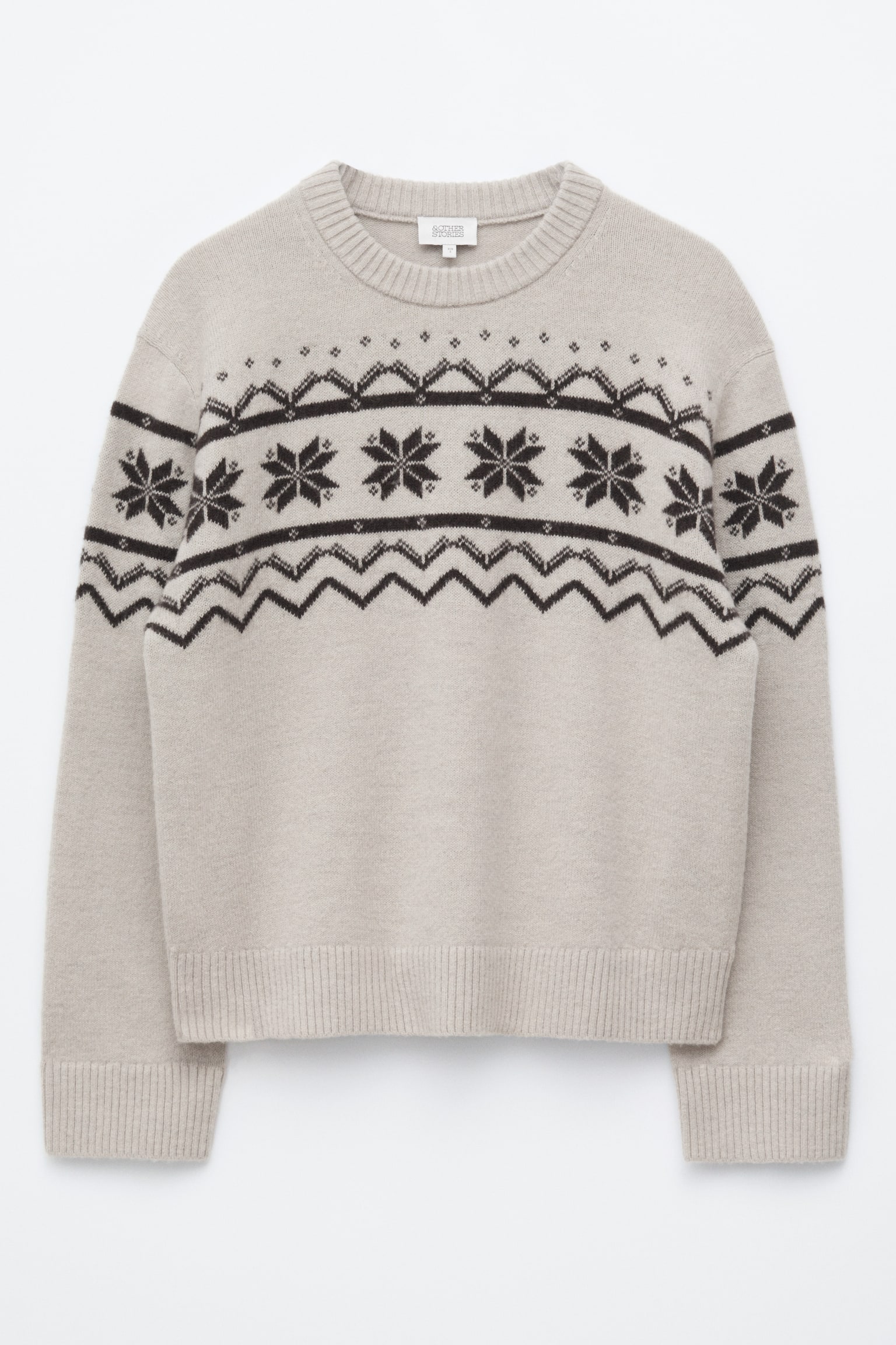 SvetlobÃ©Å¾ovÃ½ pletenÃ½ sveter je zobrazenÃ½ spredu a na hrudi a v hornej Äasti rukÃ¡vov mÃ¡ tmavohnedÃ½ vzor Fair Isle so snehovÃ½mi vloÄkami a geometrickÃ½mi motÃ­vmi. Odev mÃ¡ boxy strih a je zakonÄenÃ½ rebrovanÃ½m okrÃºhlym vÃ½strihom, rebrovanÃ½mi manÅ¾etami a rebrovanÃ½m spodnÃ½m lemom. - 1