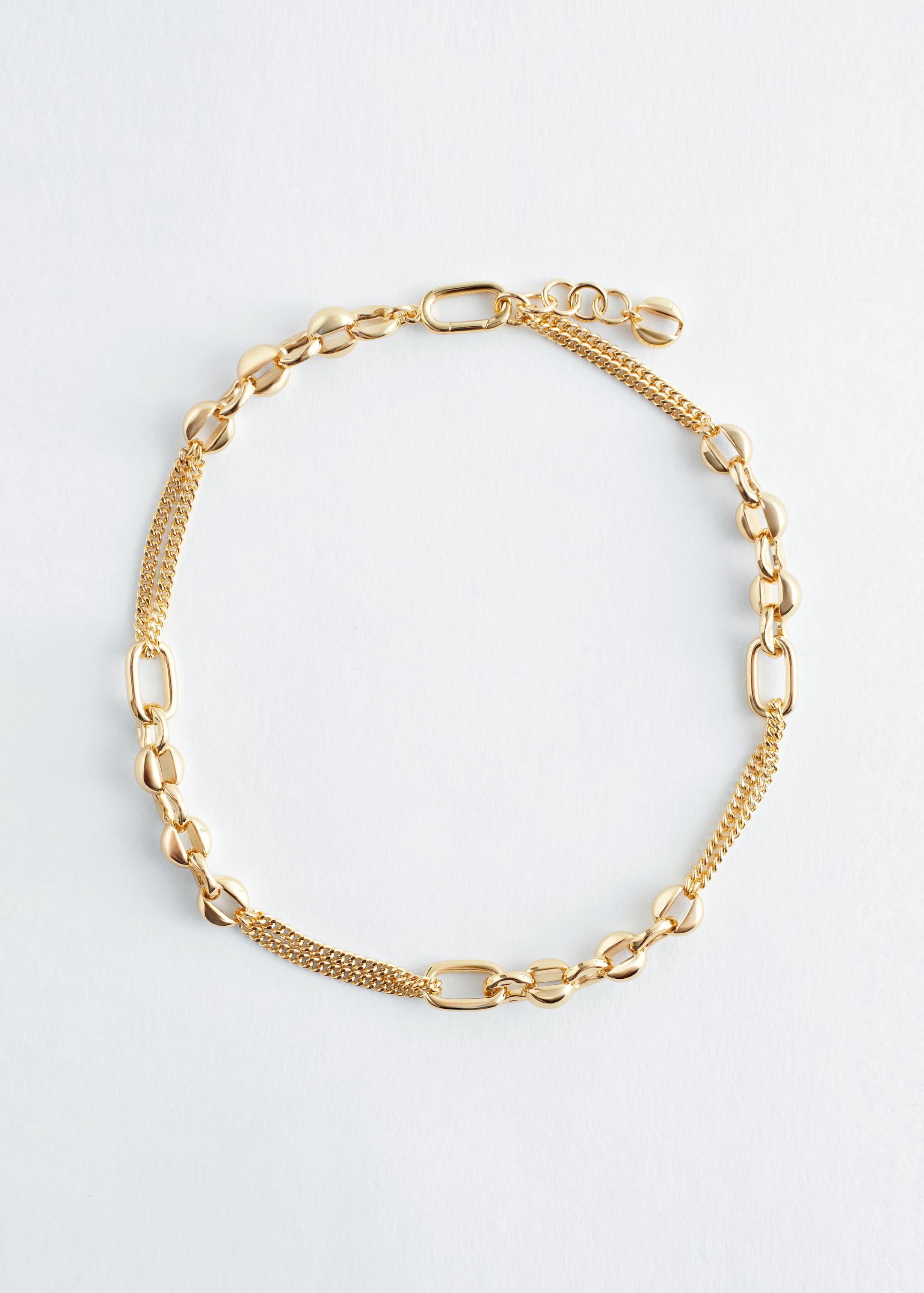 View larger image: A gold-toned necklace is lying flat in a circular arrangement, featuring a chain composed of alternating elongated oval links and smaller, puffed round links. Sections of the necklace are incorporating a double strand of fine curb chain, and it is finished with an oval-shaped spring clasp and an extension chain.
