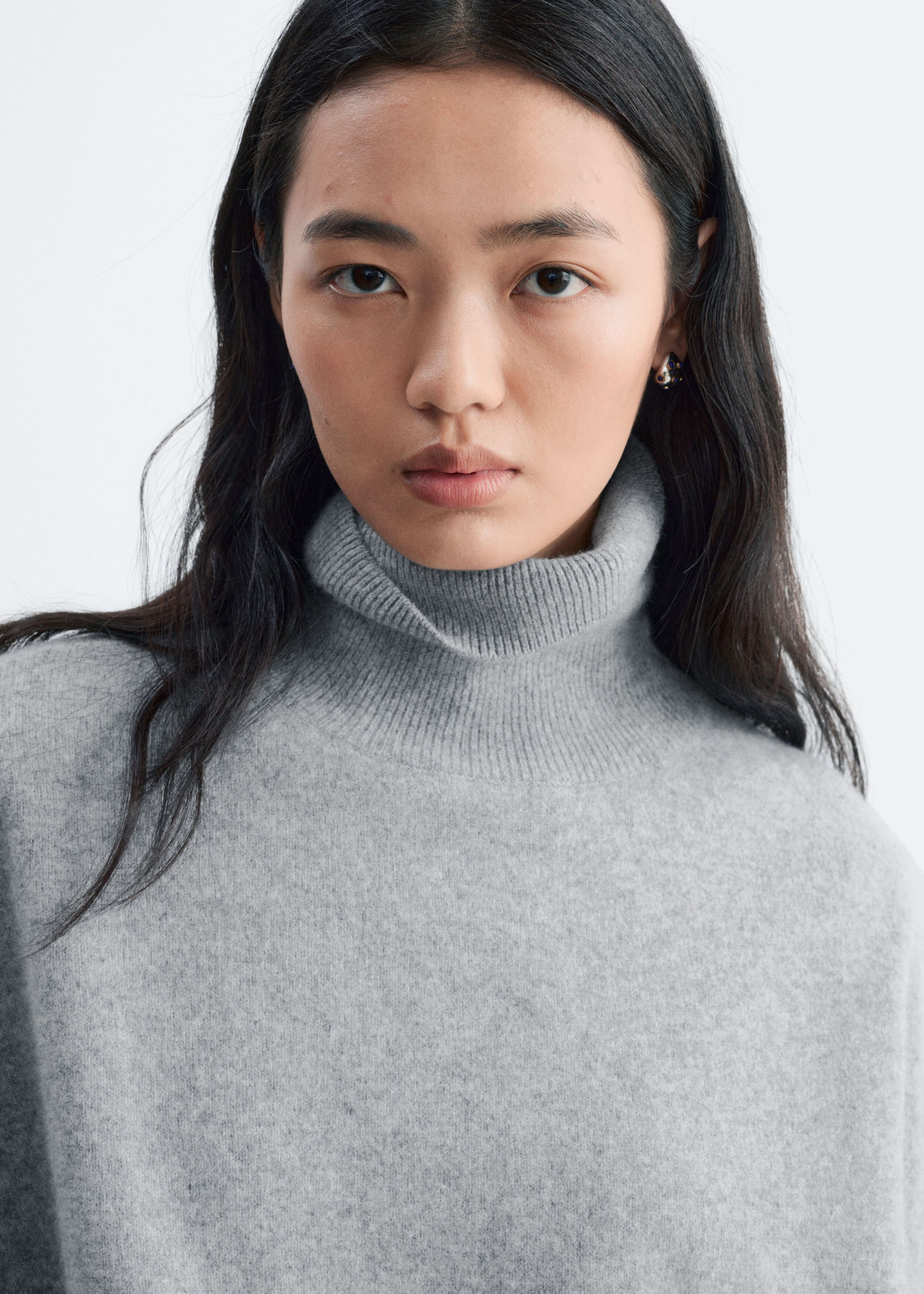 A light grey knitted jumper featuring a folded ribbed roll neck is being worn by the model. The close-up view is highlighting the soft, textured knit of the garment.