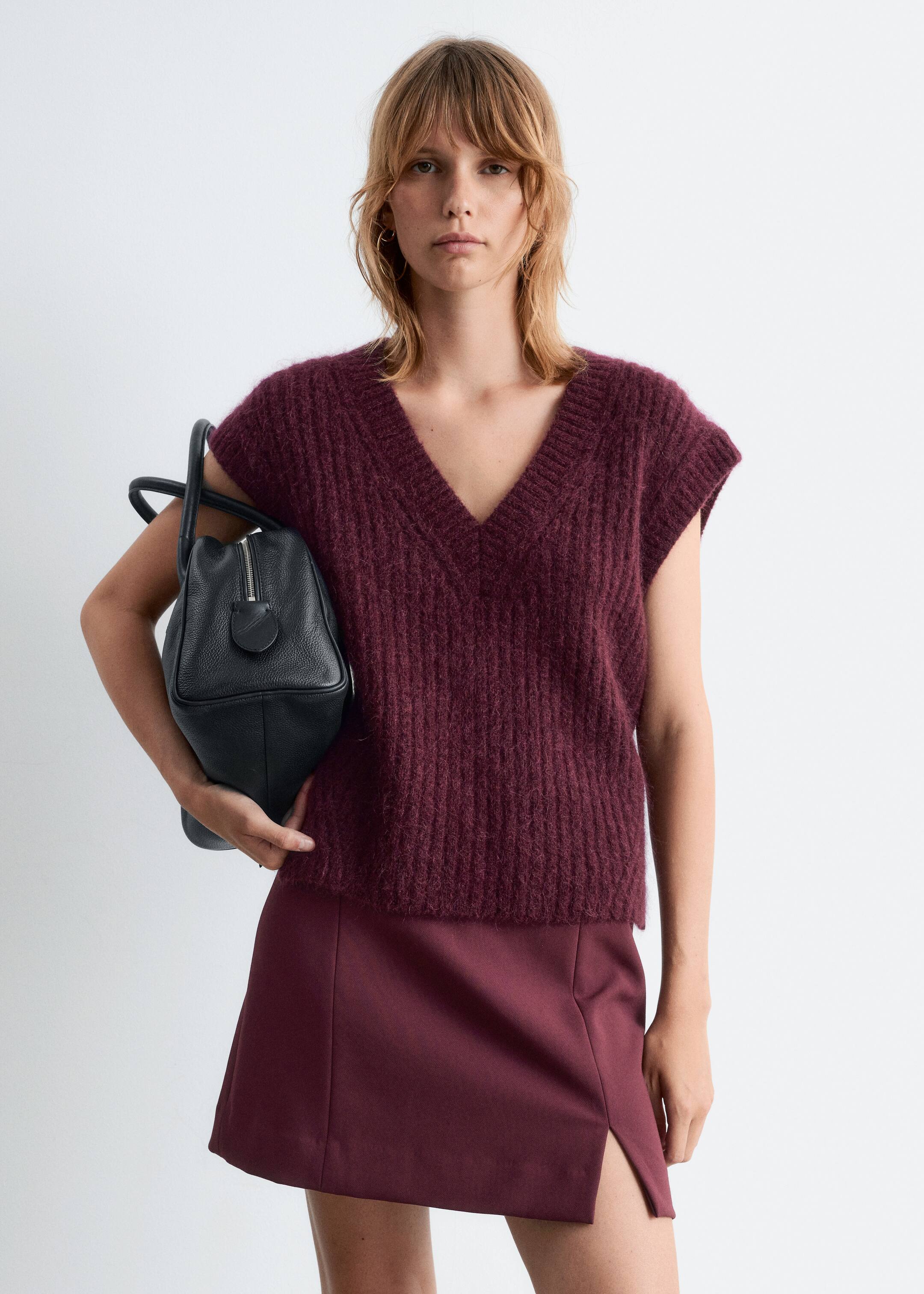 View larger image: A front-facing, burgundy V-neck sleeveless sweater, featuring a fuzzy, ribbed knit texture, is being paired with a matching burgundy mini-skirt that is designed with a side slit.