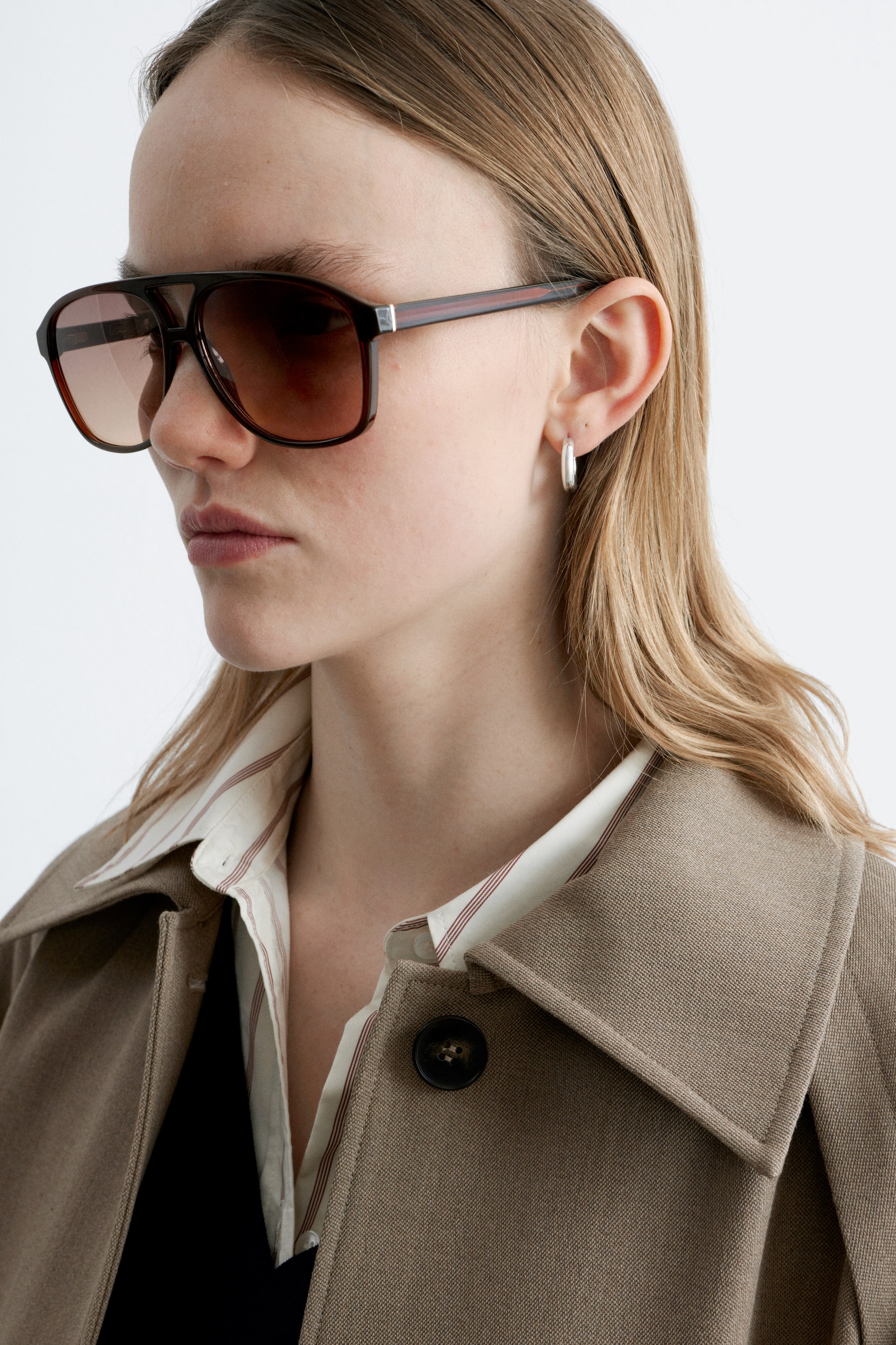 Visa större bild: Överdimensionerade solglasögon i aviator-stil bärs, sedda från en främre vinkel, med rundade kanter, en klassisk brynbar och smala, mörkbruna bågar med ett subtilt randmönster. Linserna är tonade med en brun gradient, och en silverfärgad detalj är synlig på skalmarna nära gångjärnen.