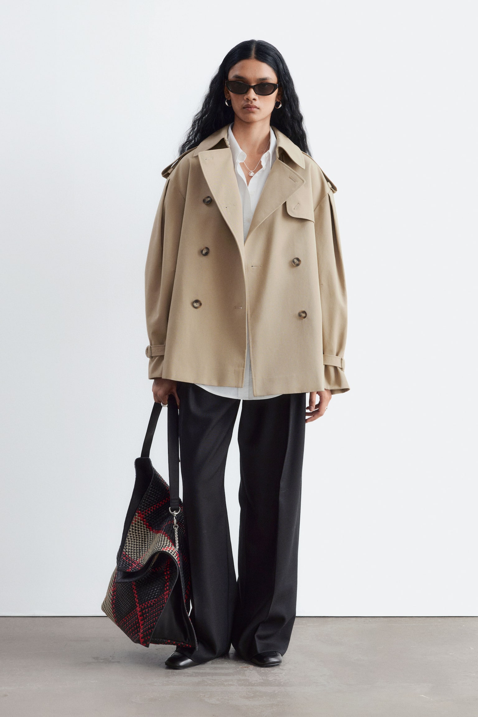 Un trench scurt bej este purtat de model, peste o cÄmaÈÄ albÄ cu guler Èi pantaloni negri evazaÈi cu croialÄ largÄ. Paltonul cu douÄ rânduri de nasturi are revere late crestate, epoleti pe umeri Èi detalii cu cureluÈe la manÈete. - 1