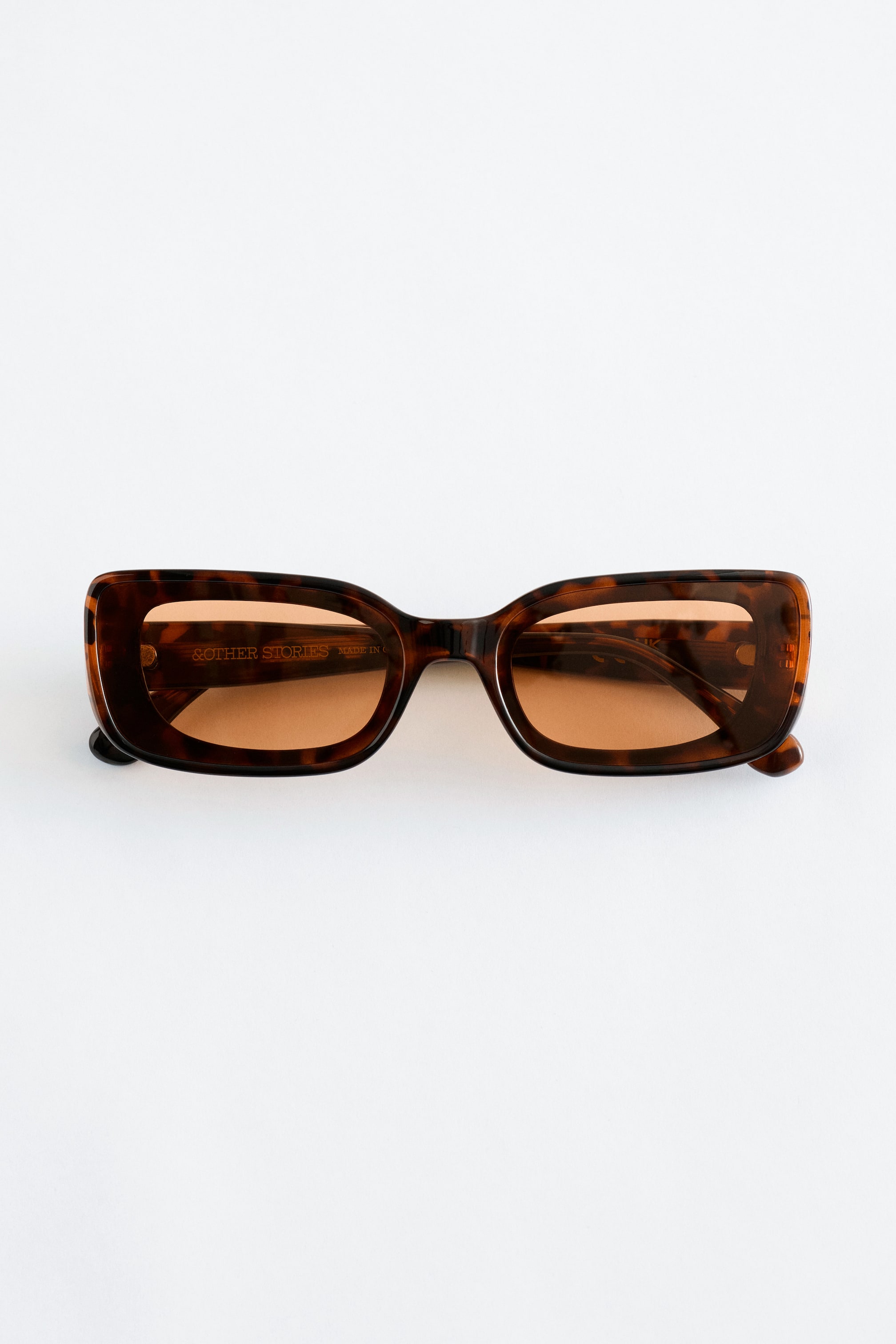 View larger image: A pair of tortoiseshell rectangular sunglasses is lying flat, facing front, featuring wide frames, wide temples, and amber-tinted lenses.