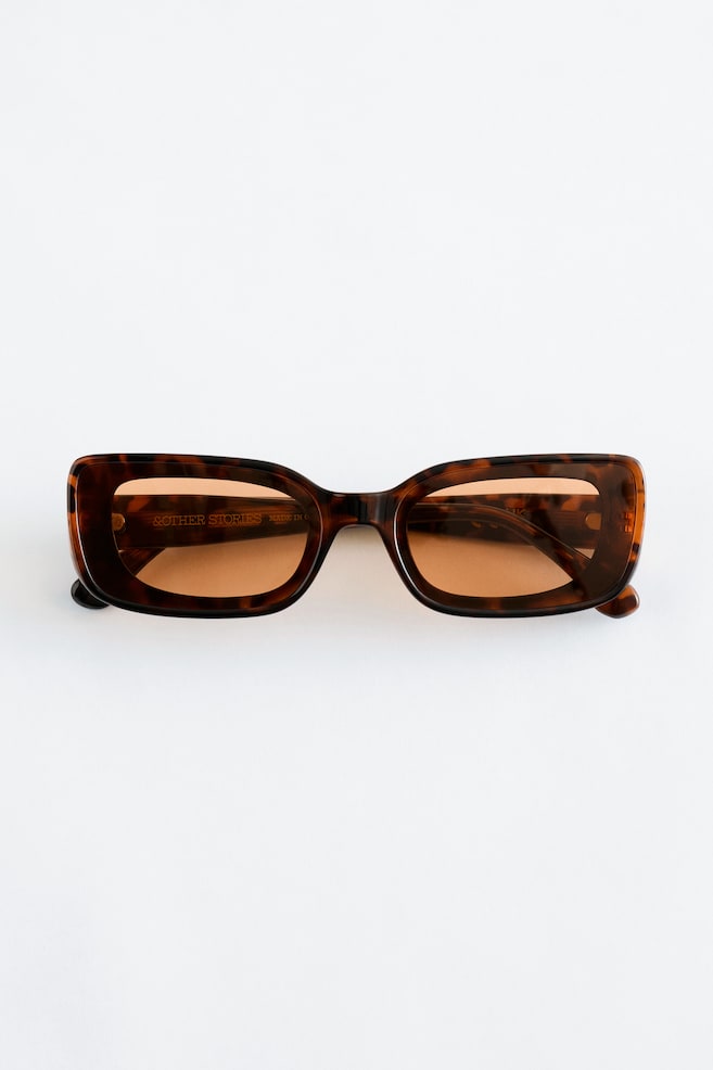 A pair of tortoiseshell rectangular sunglasses is lying flat, facing front, featuring wide frames, wide temples, and amber-tinted lenses. - 1