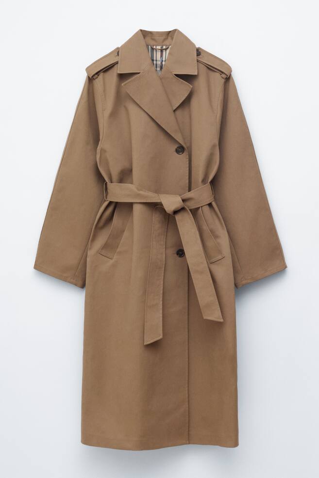Een camel trenchcoat toont zijn voorkant, met gekartelde revers, schouderriempjes en een ceintuur van dezelfde stof die in de taille is vastgebonden. Donkere knopen zijn zichtbaar op de voorkant van de sluiting, en een geruite voering is te zien in de binnenkraag. - 1